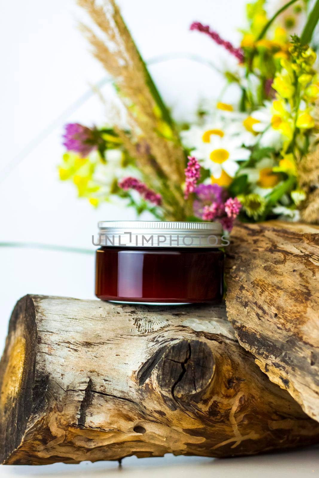 a jar of cream on the background of a dry stump, tree bark and a bouquet of wild flowers. Stylish appearance, layout, personality. Banner, a place for the text. Background for advertising and presentation.