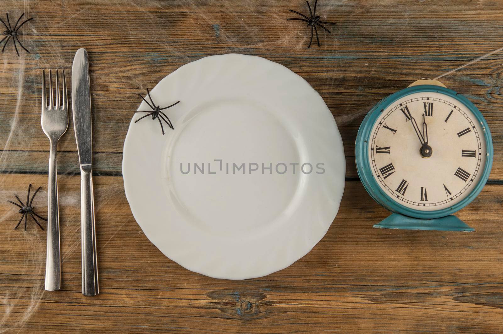 Halloween table setting blank dish, knife and fork with spider web on wood background. Flat lay, top view trendy holiday concept. by inxti