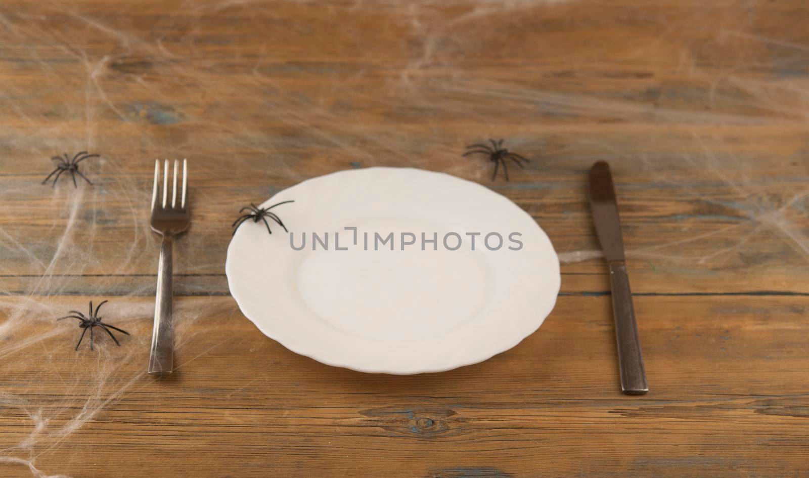 Halloween table setting blank dish, knife and fork with spider web on wood background.Trendy holiday concept.