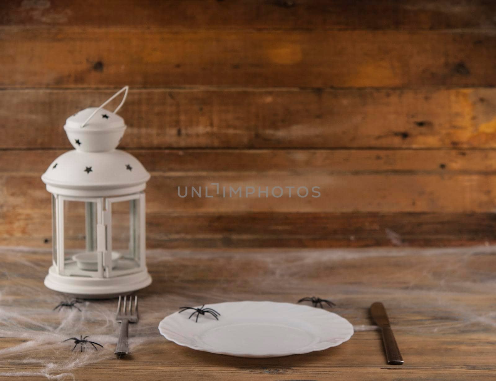 Halloween table setting blank dish, knife and fork with spider web on wood background.Trendy holiday concept.