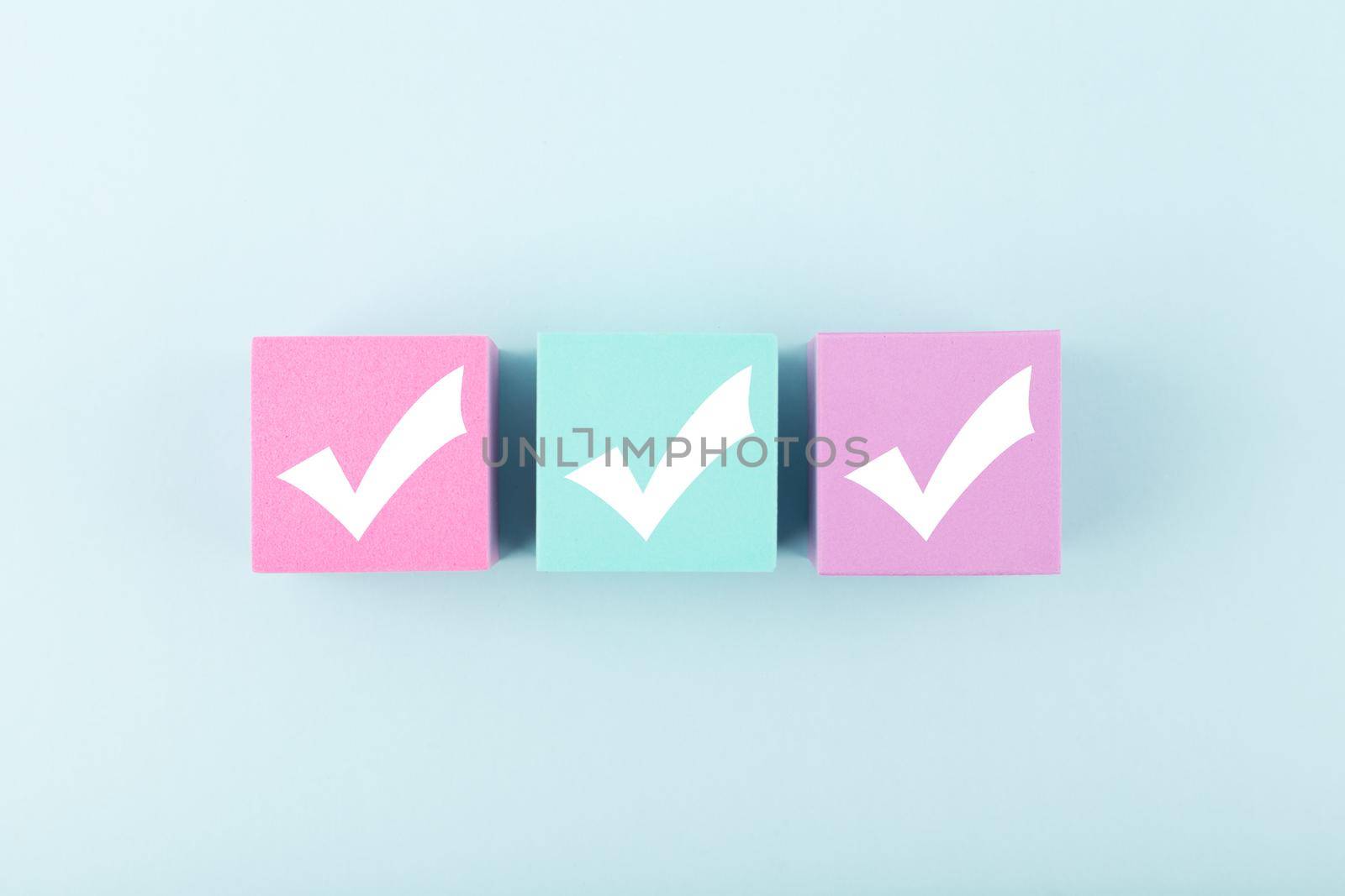 Three checkmarks on multicolored cubes in a row in the middle of bright pastel blue background. Concept of questionary, checklist, to do list, planning, business or verification. Modern minimal composition 