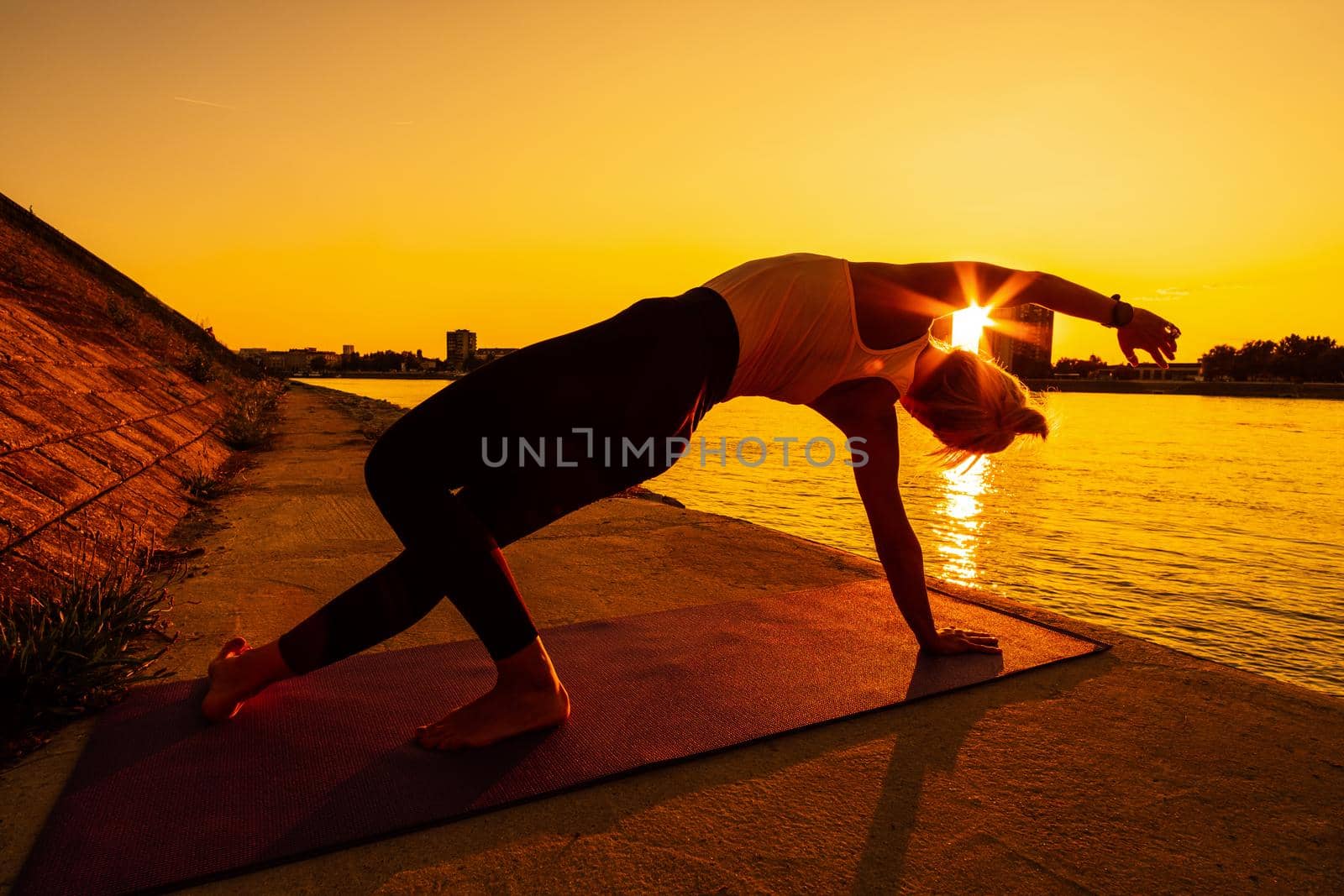 Young woman is exercising outdoor. She is practicing yoga on sunny day. Camatkarasana, Wild Thing yoga pose.