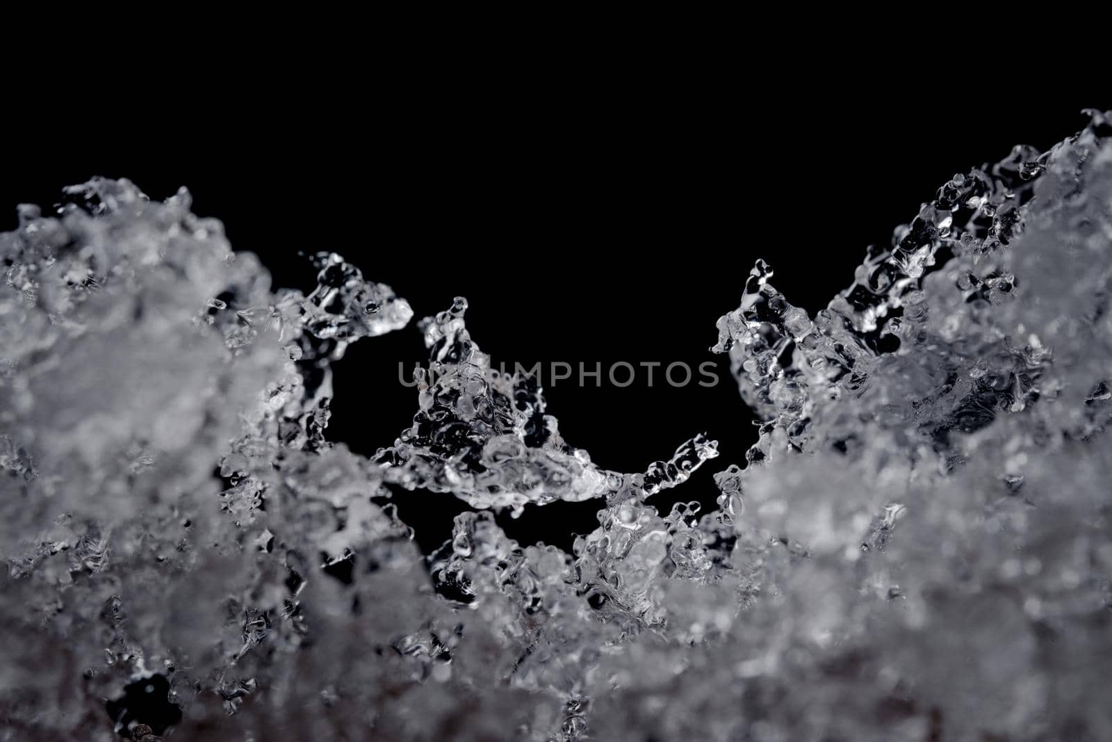 Intricate details of melting water particles. Focus on odd shaped ice crystal in the middle, but plain black background with copy space above.