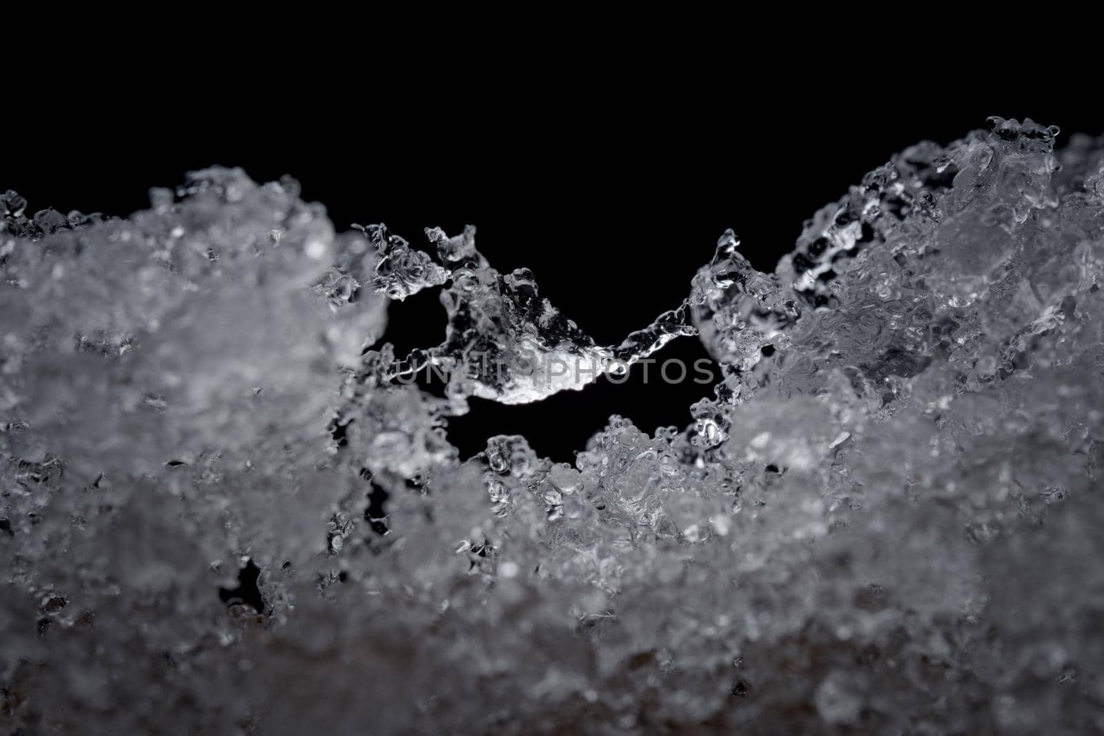 Super close up abstract image of slowly thawing snow. Minute detail of the ice crystals are visible, plain black background. Cold outdoor weather