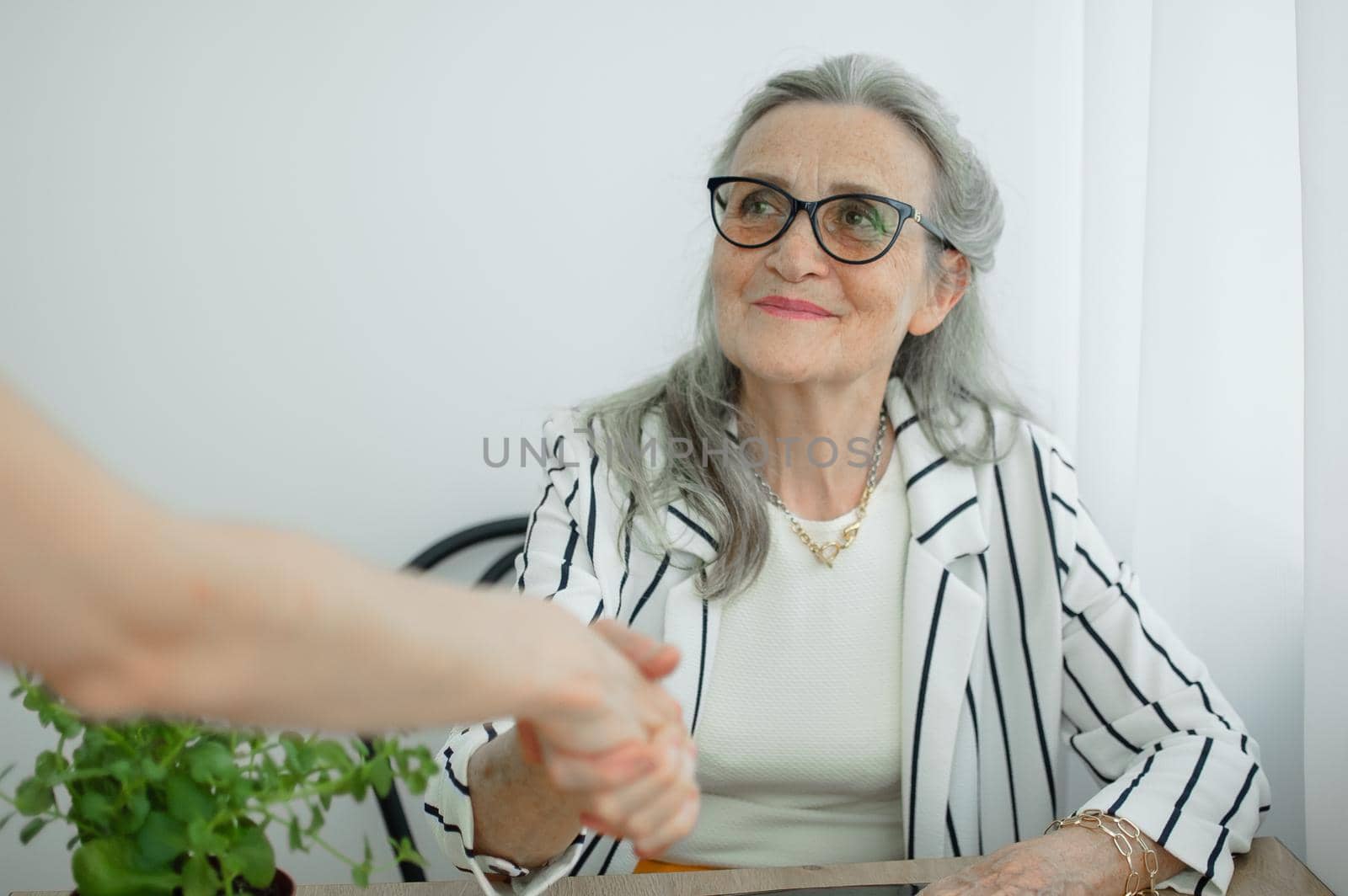 Mature businesswoman is leading an interview with new colleague and shaking their hand at the end. Business people concept.