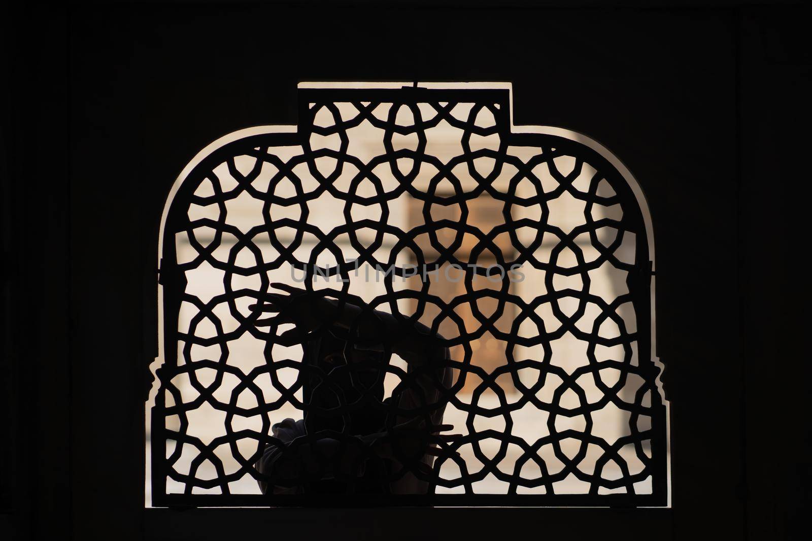 A Muslim girl in a black hijab stands behind a patterned wrought-iron fence. Woman in a conservative Arab country.
