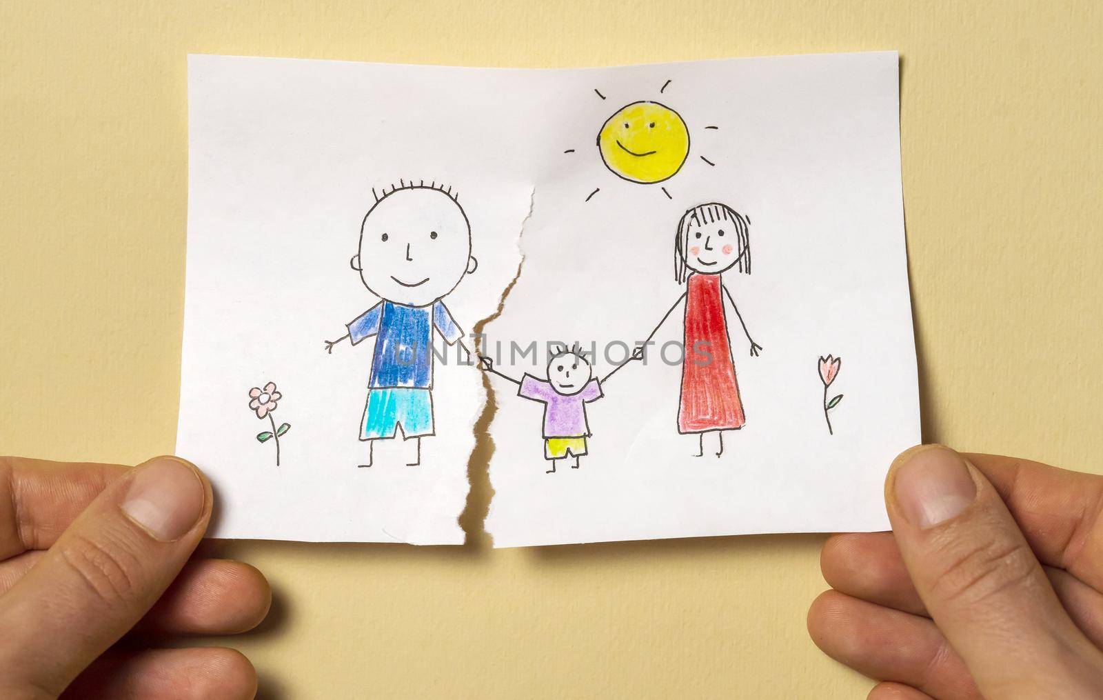 A child's drawing, which depicts a mom, dad and a child, is torn in half by man's hands. Divorce, relationship difficulties, child problems.