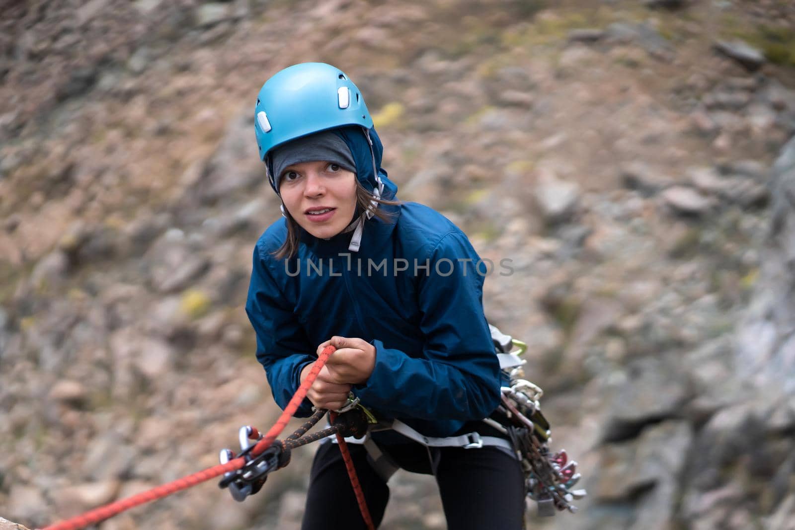 Traveler with mountaineering equipment and a helmet descends from the top of the mountain on a rope, view from above. Young cute girl with funny expression is engaged in climbing.