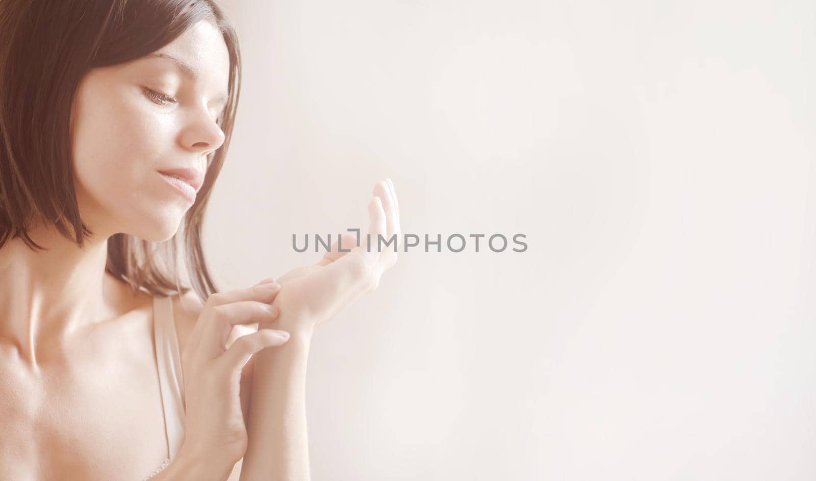 A young girl takes care of the health of her skin in the bathroom, a woman looks at her gentle moisturized hands on a light background.