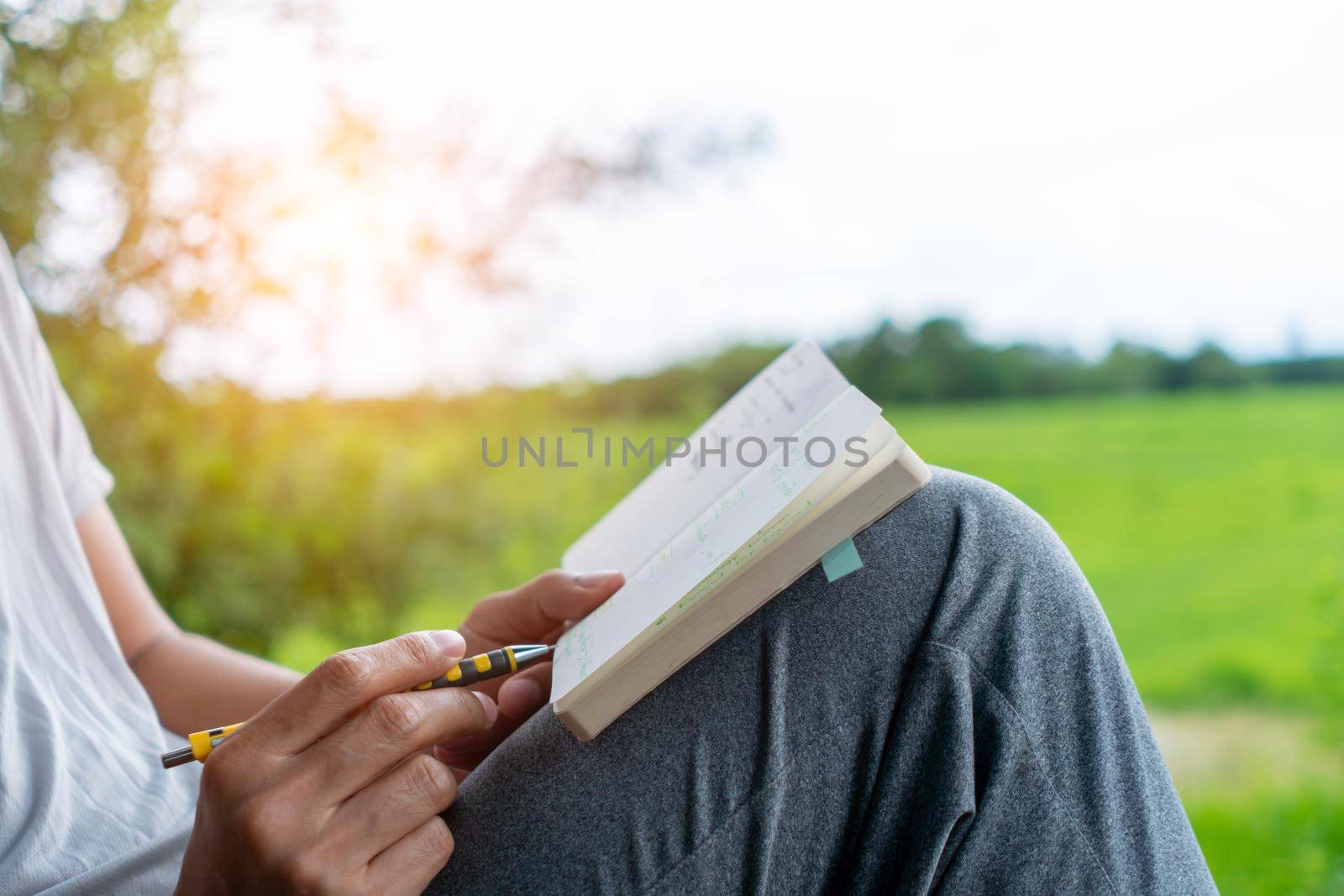 In a public park, a man is handwriting in a small white memo pad to make a note of something he doesn't want to forget or to make a to-do list for the future concept.