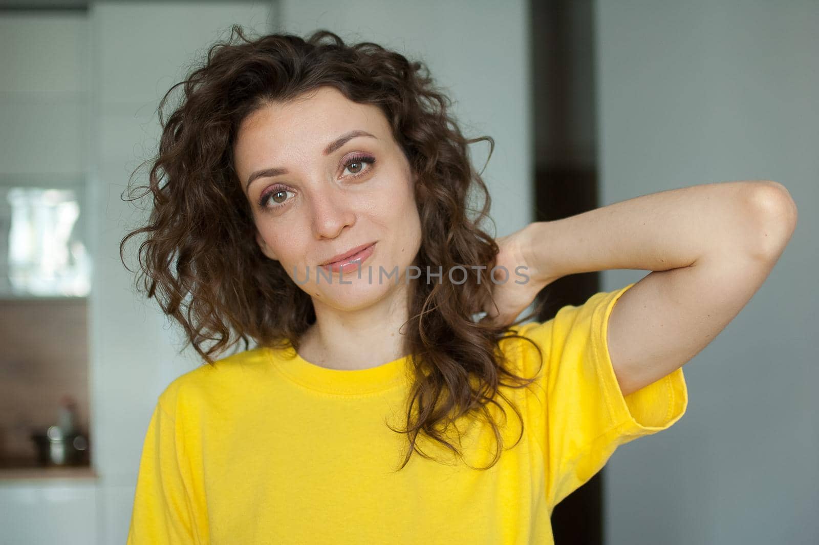 Beautiful curly girl in yellow t-shirt is looking at the camera at home in her apartment, posing with smile, happy people concept by balinska_lv