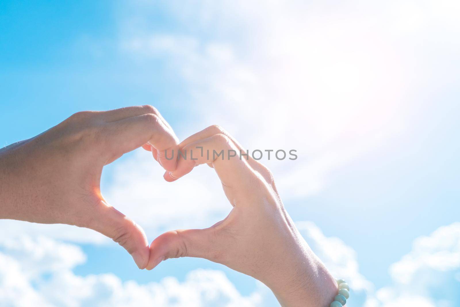 Woman hand do heart shape on blue sky and beach background.