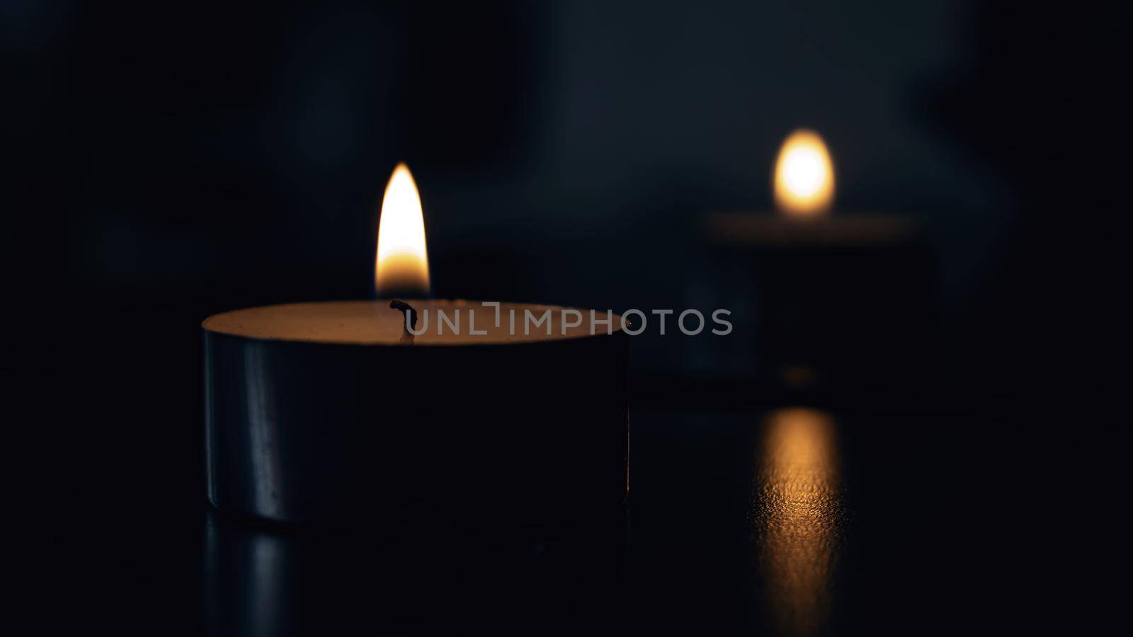 Flame of a small candle in the dark with reflection