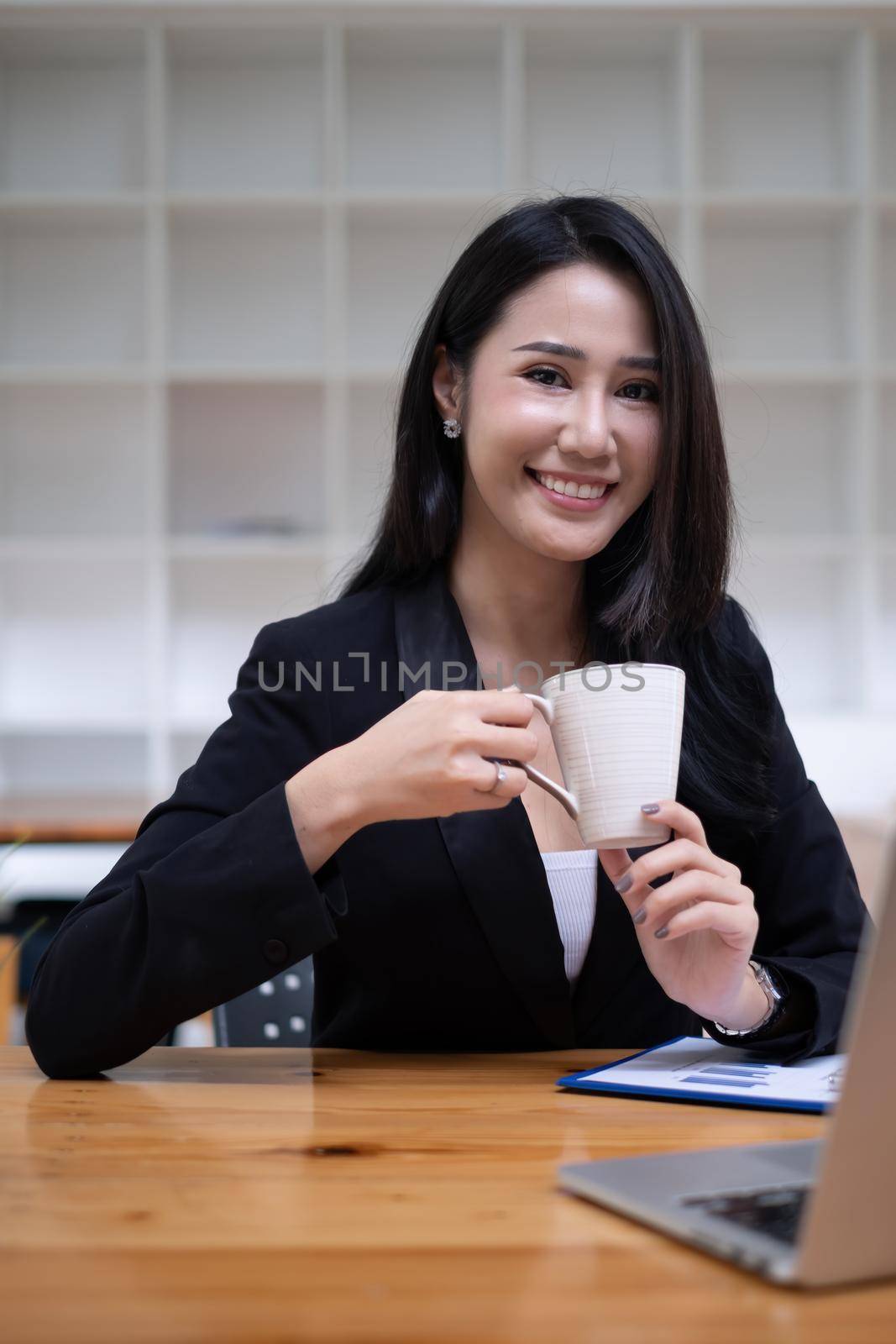 Portrait of cheerful asian woman looking camera and tablet on desk in office. Concept of young business people by itchaznong