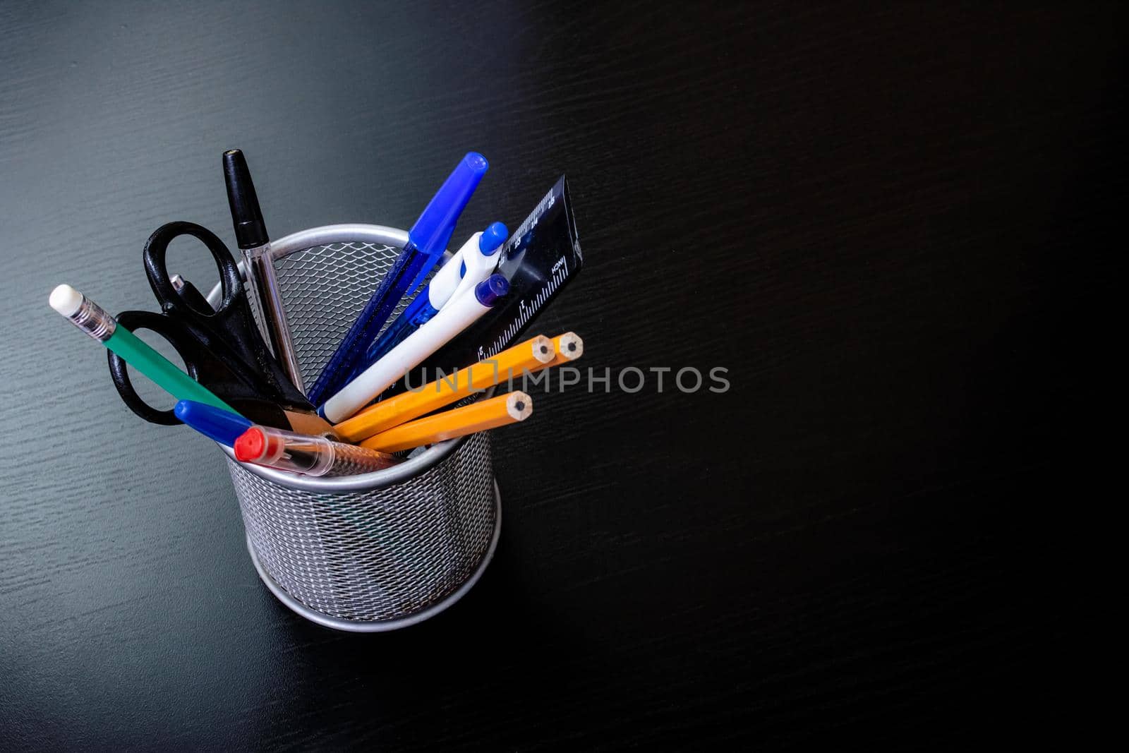 Metal stand with pencils, pens, scissors on a black wooden table close up