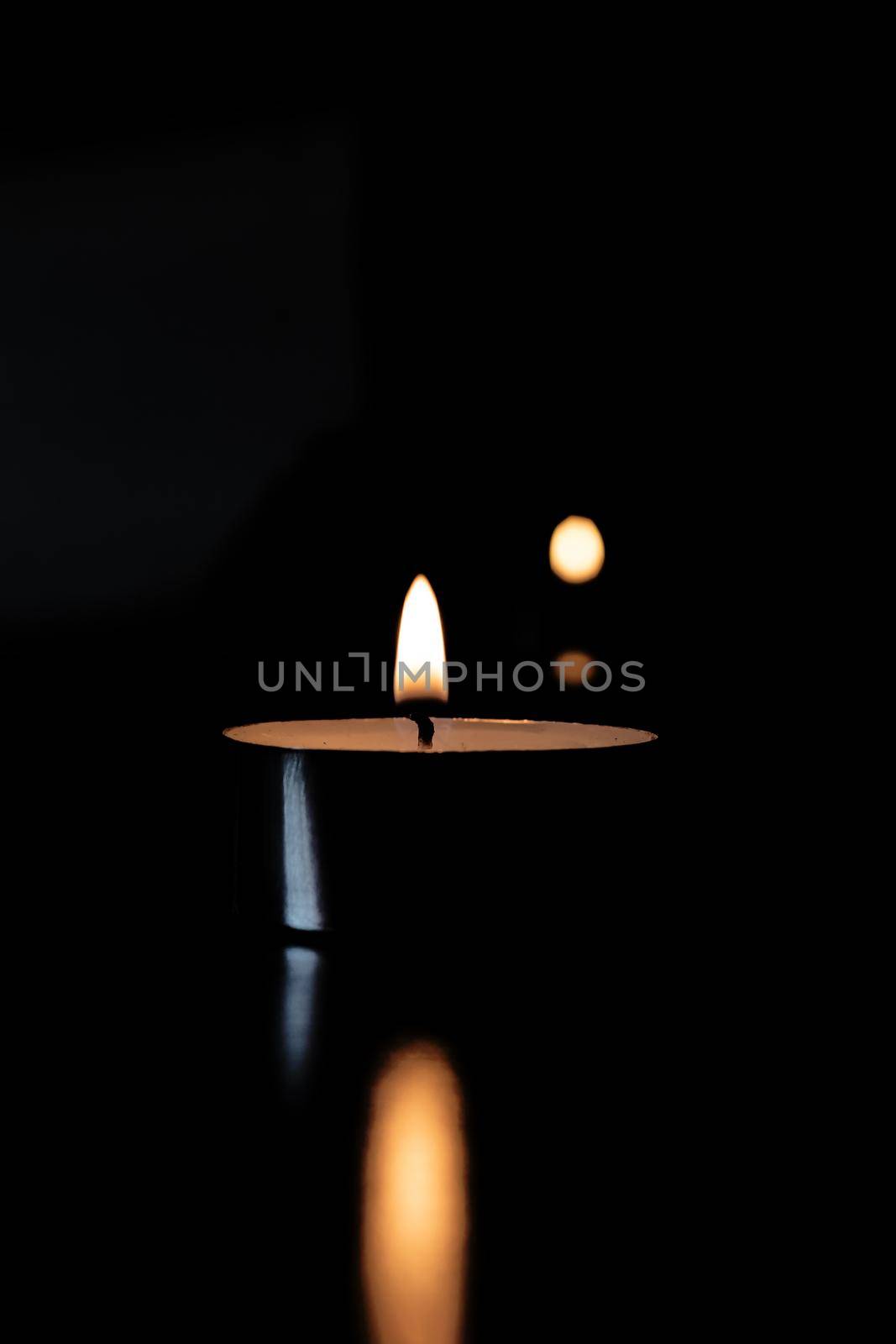 Flame of a small candle in the dark with reflection