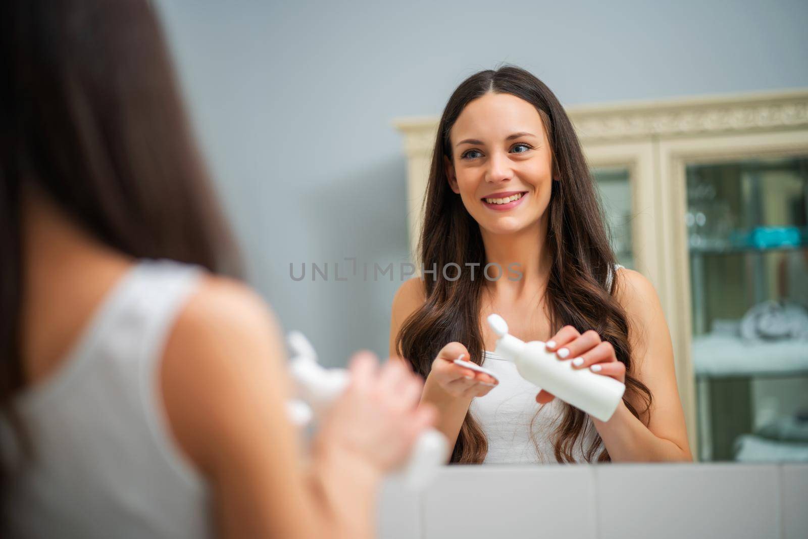 Portrait of young woman who is applying skin cream.
