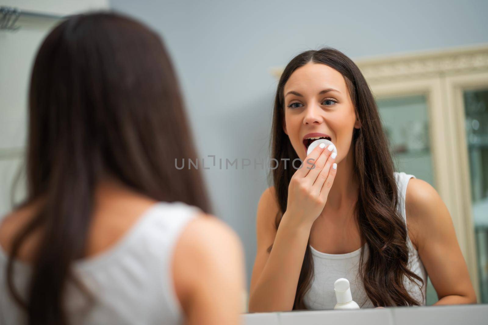 Portrait of young woman who is cleaning skin on her face.