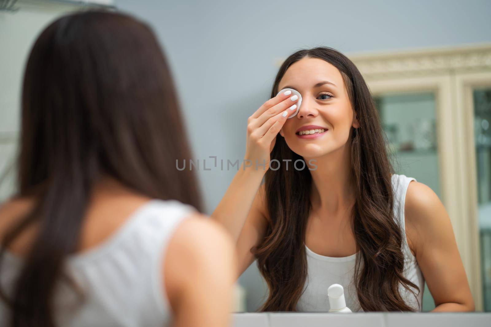 Portrait of young woman who is cleaning skin on her face.