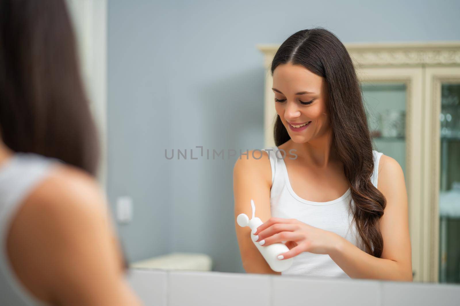 Portrait of young woman who is applying skin cream.