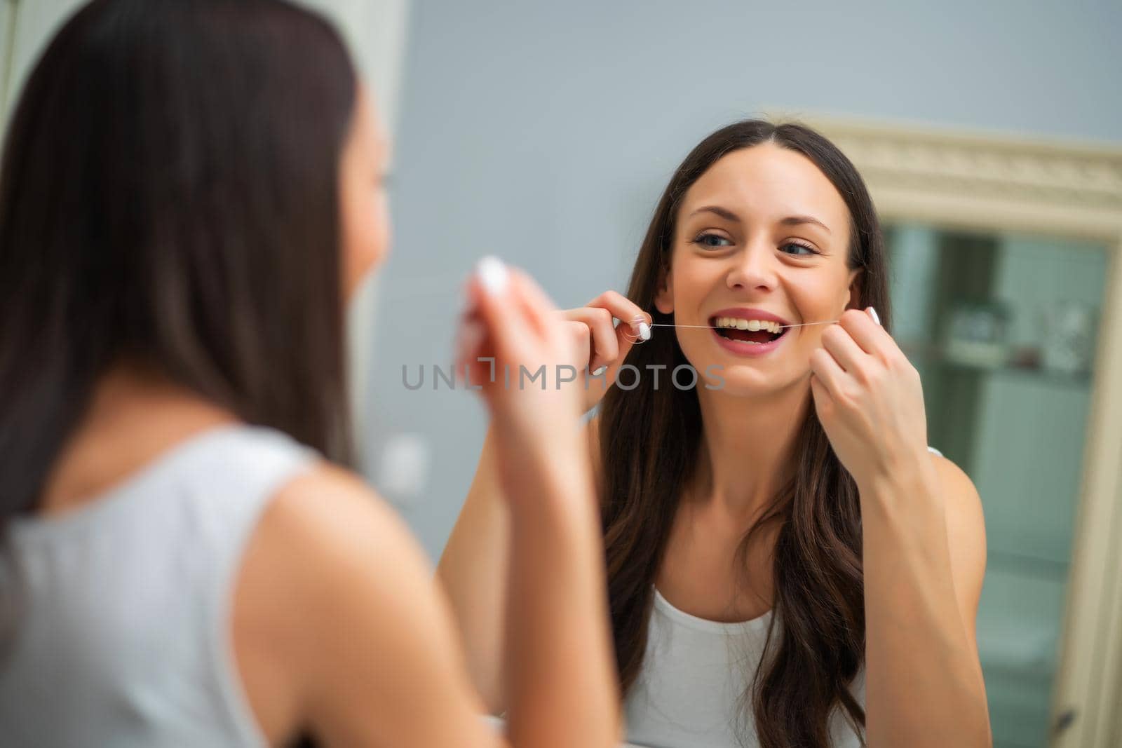 Young woman is using dental floss to clean her teeth.