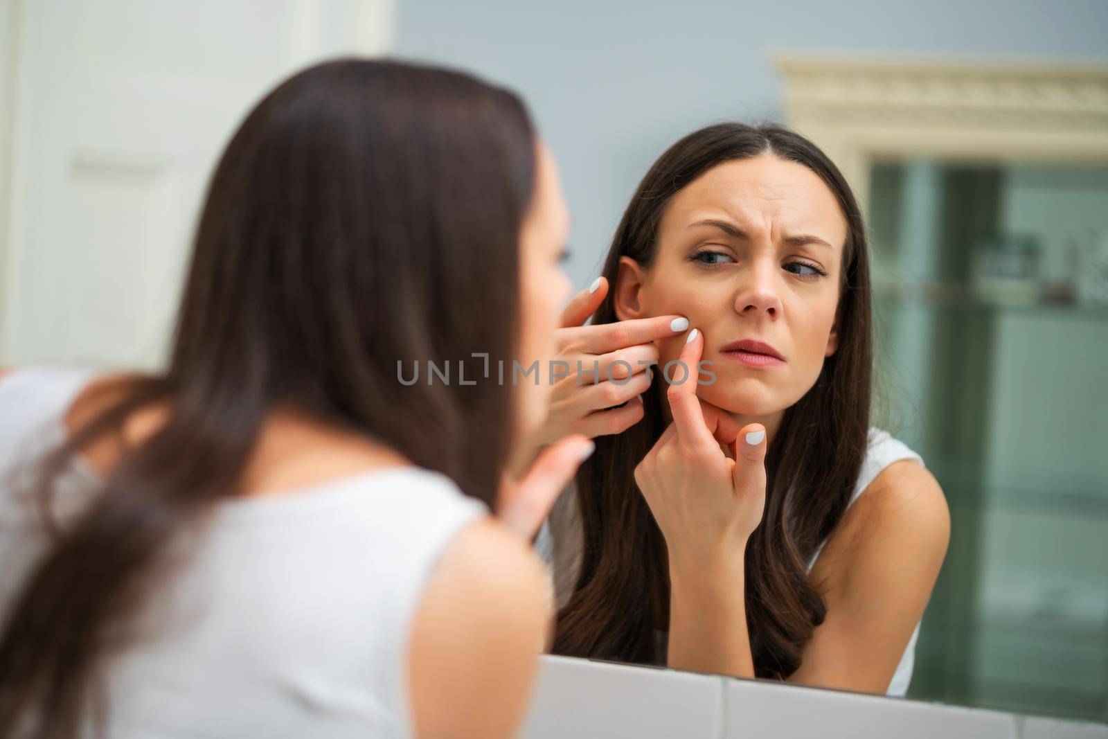 Young woman is squeezing pimple in the bathroom.