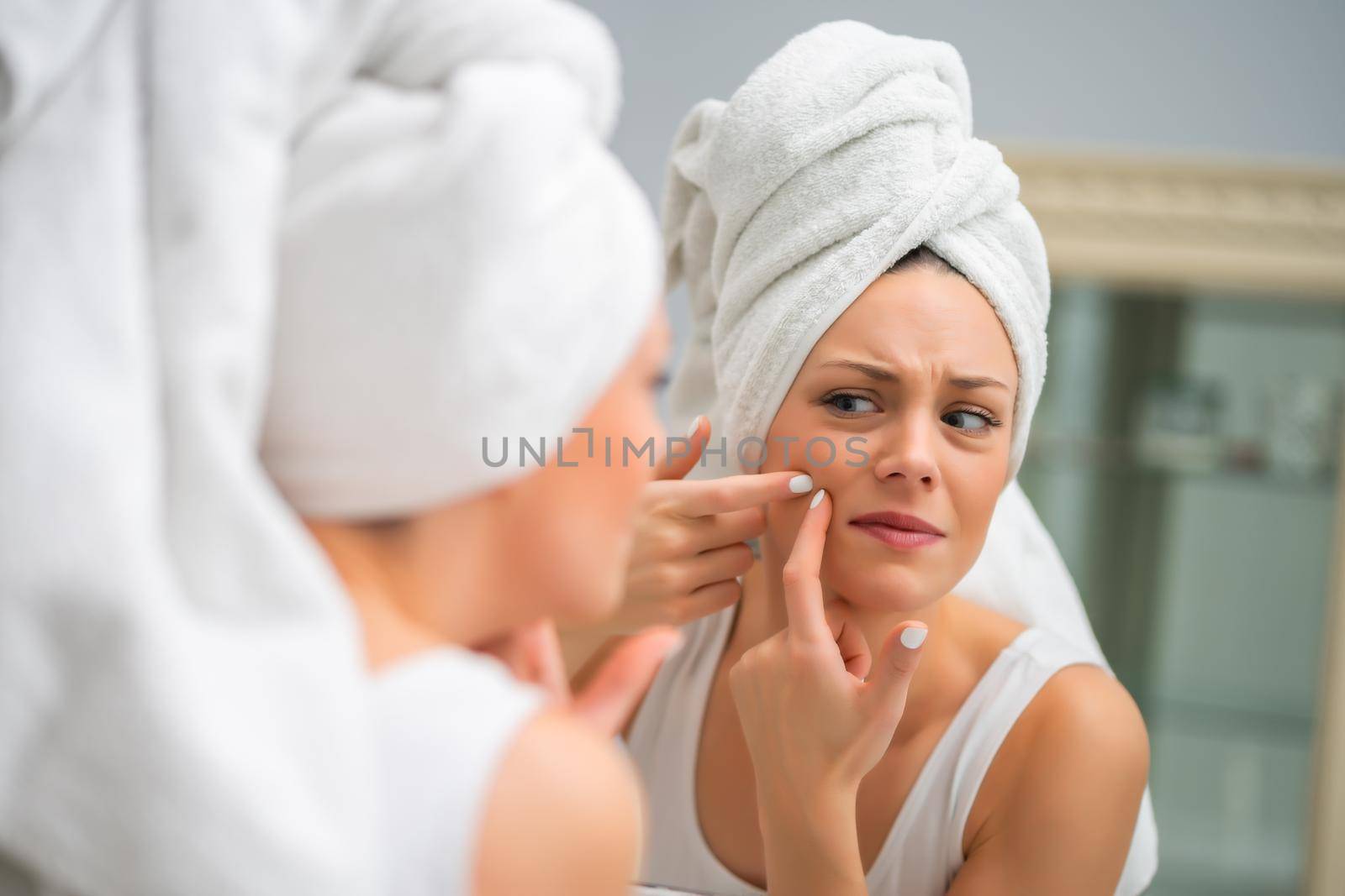 Young woman is squeezing pimple in the bathroom.