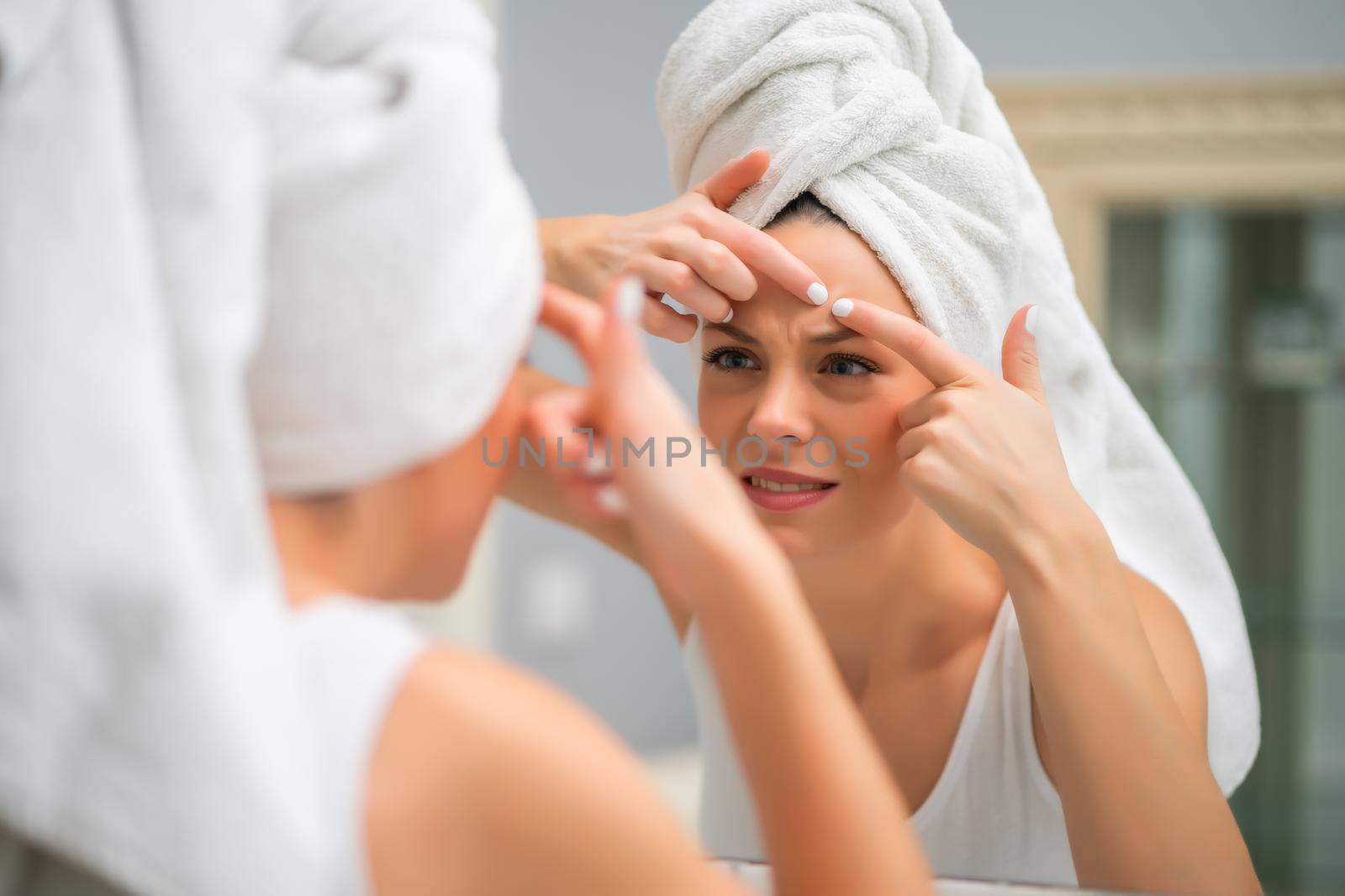 Young woman is squeezing pimple in the bathroom.