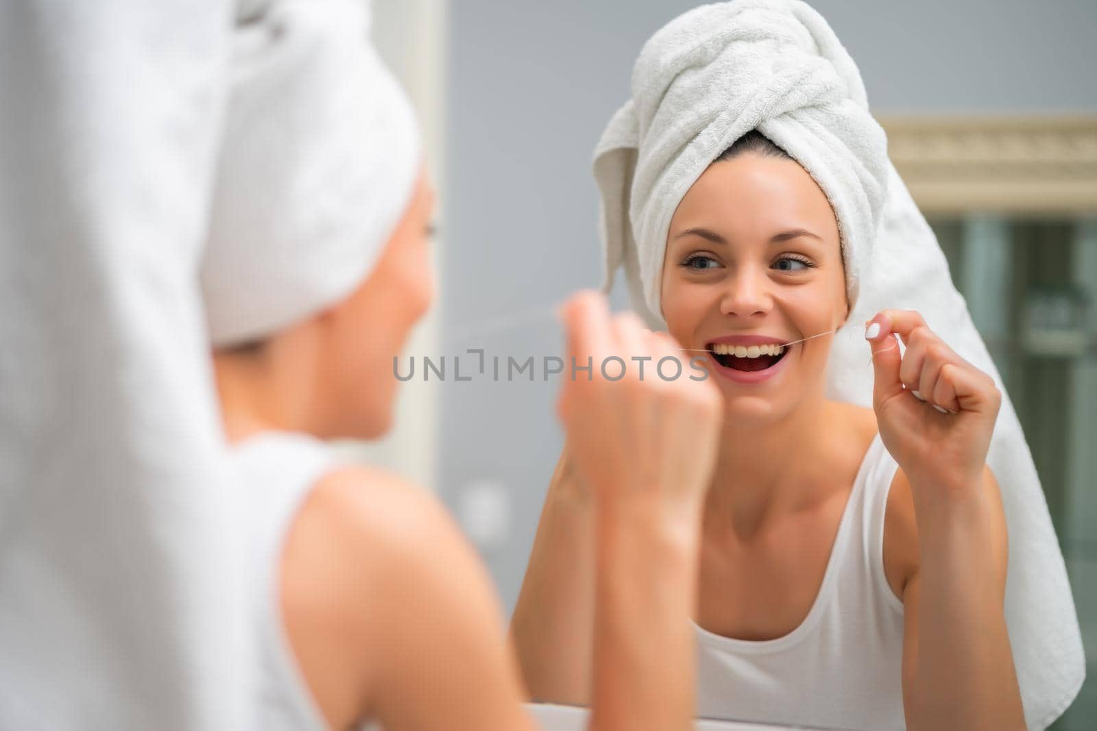 Young woman is using dental floss to clean her teeth.