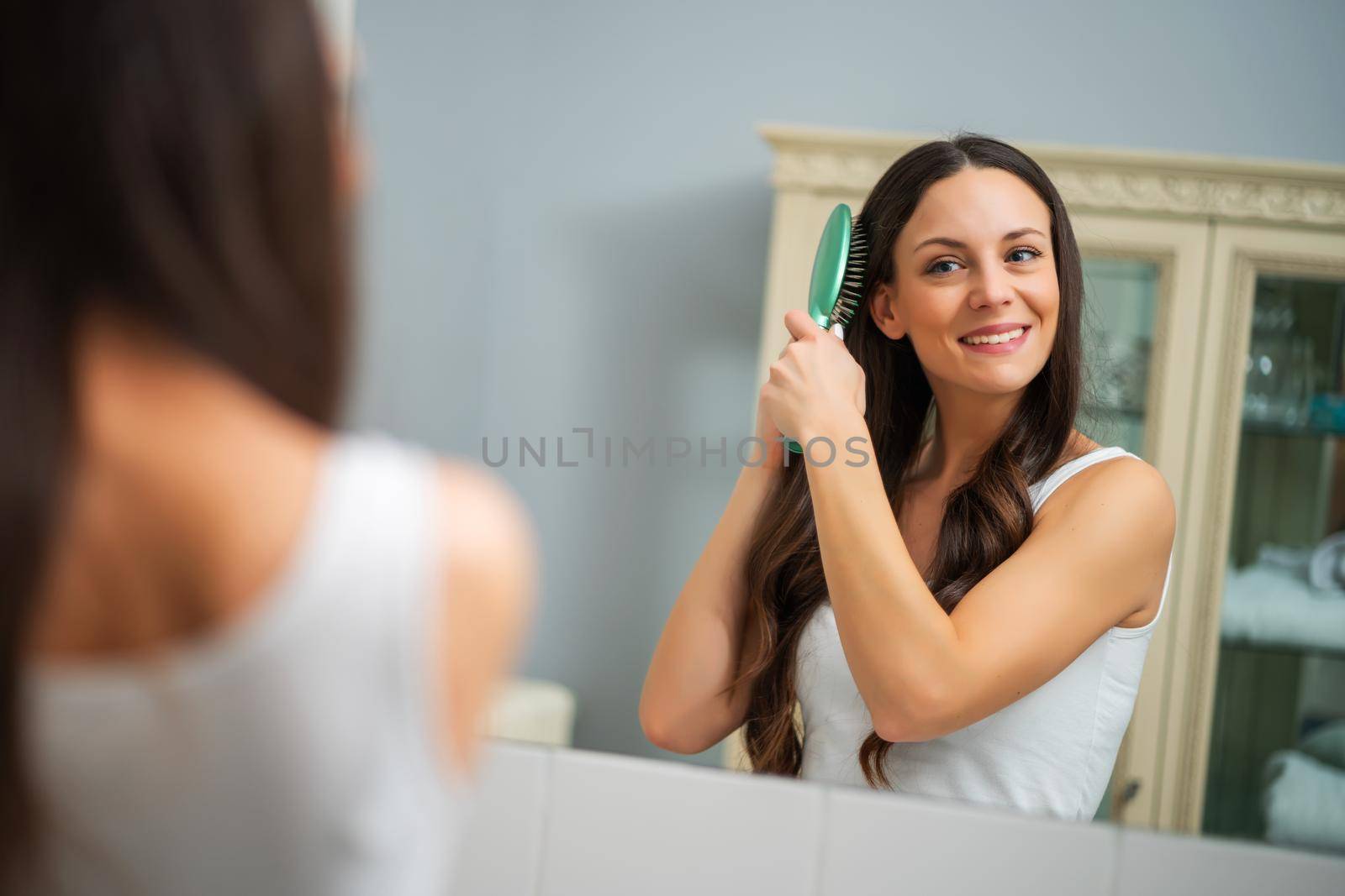 Portrait of young happy woman who is brushing her hair.