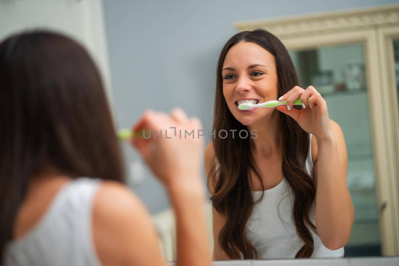 Young woman is brushing her teeth in bathroom.