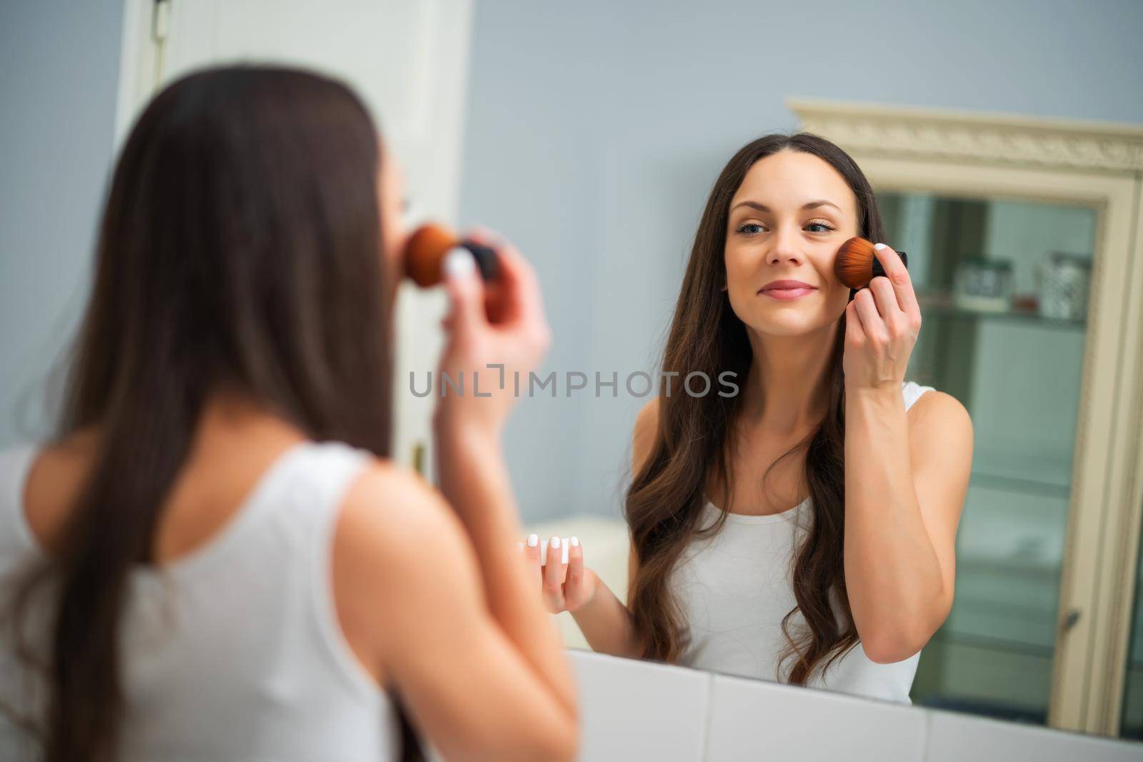 Young woman is applying blush in the bathroom.