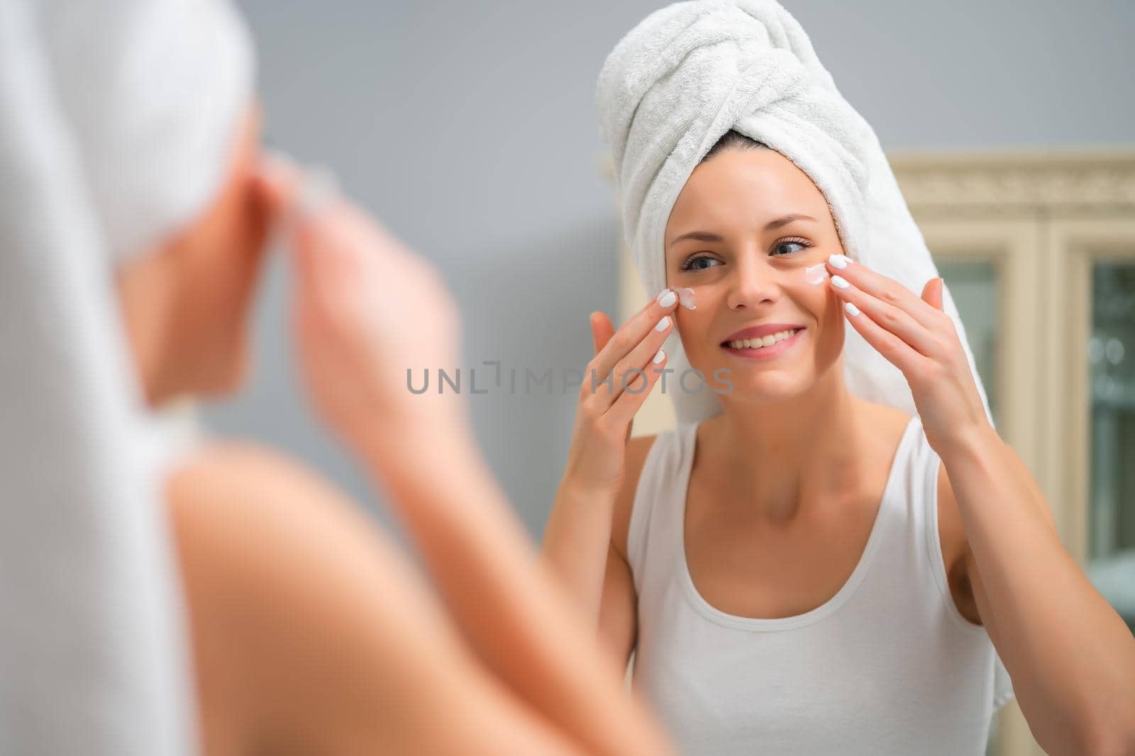 Portrait of young woman who is applying skin cream on her face.