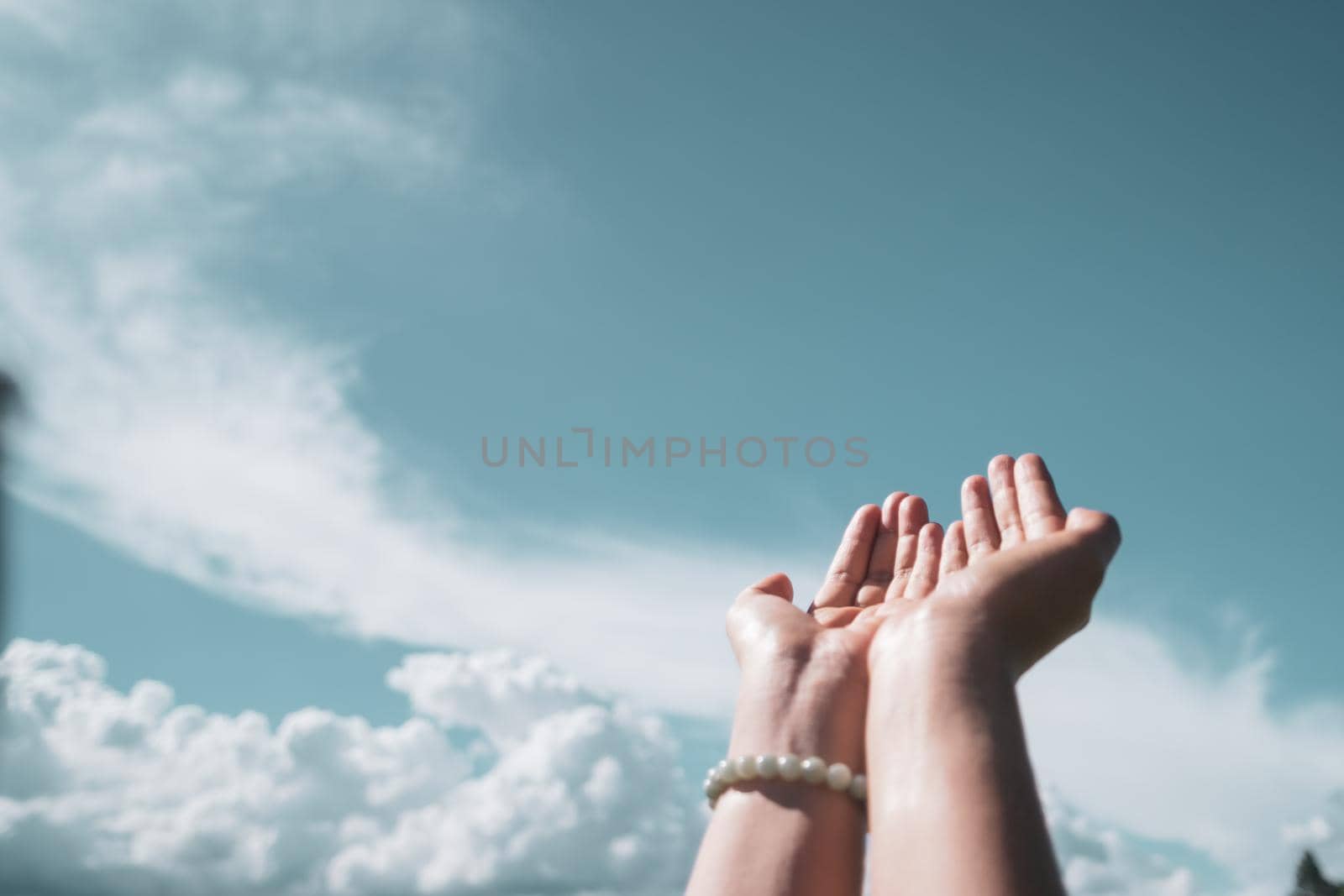 Woman hands place together like praying in front of nature blue sky background.