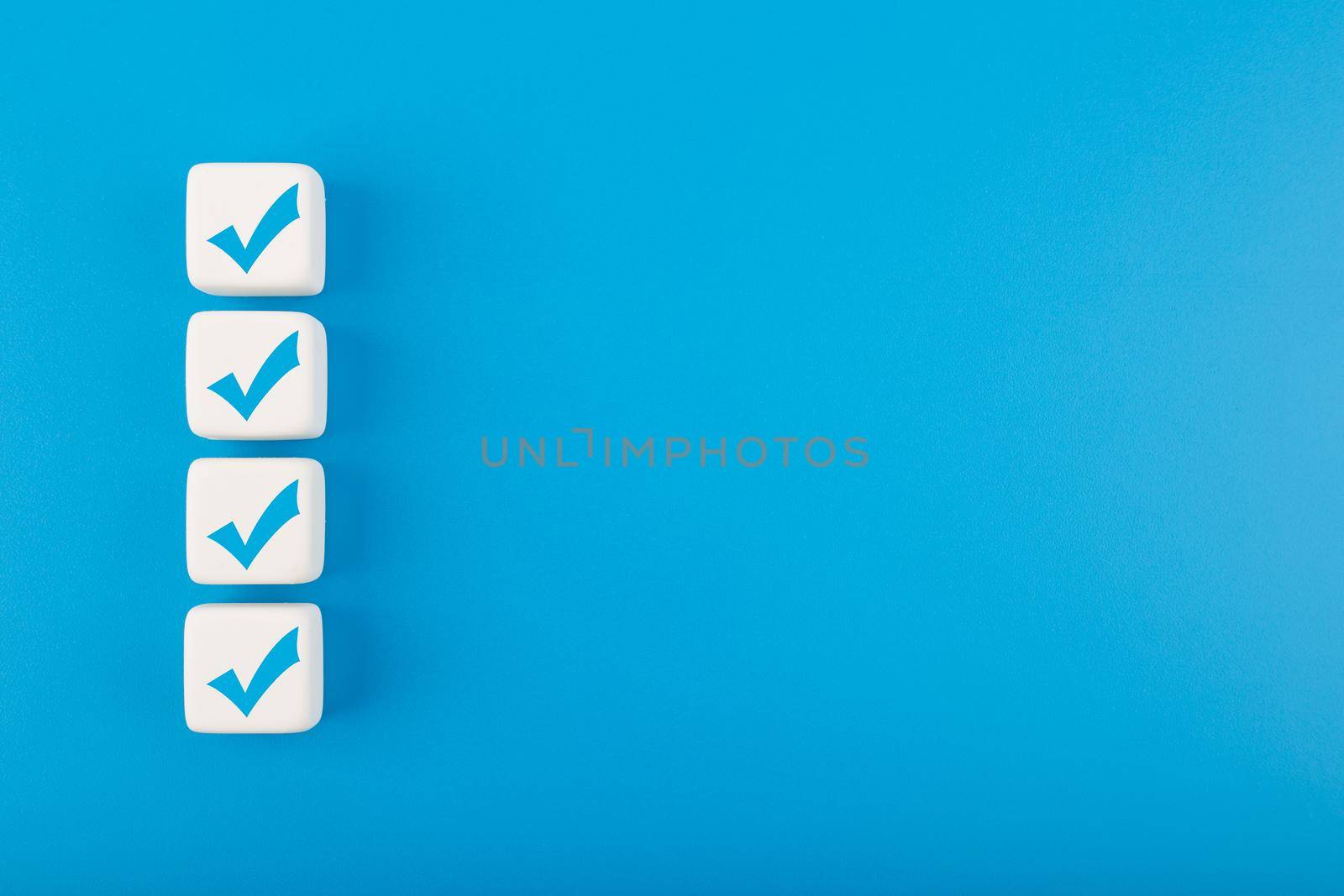 Four blue checkmarks on white cubes in a row against blue background with copy space. Concept of questionary, checklist, to do list, planning, business or verification. Modern elegant flat lay