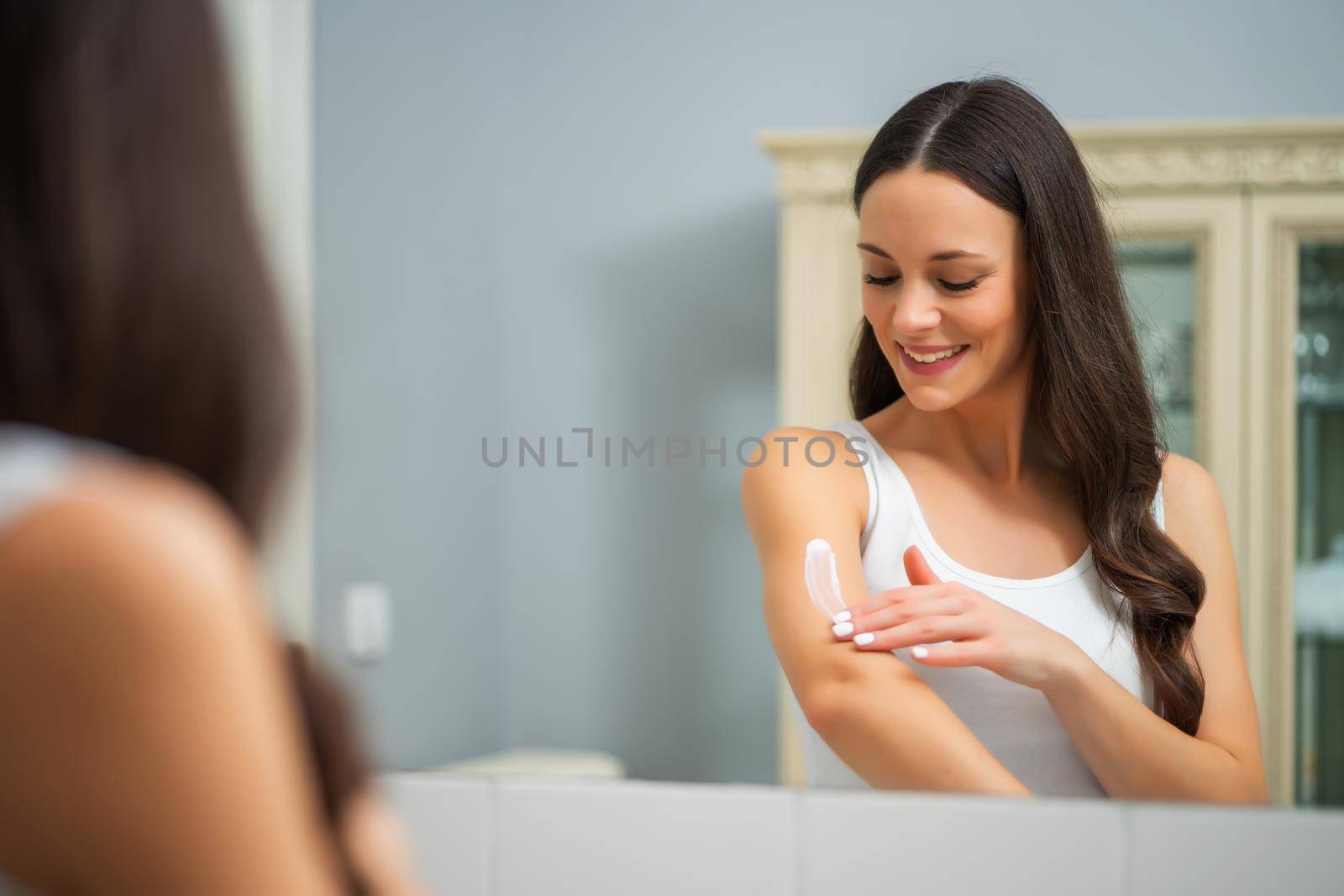 Portrait of young woman who is applying skin cream.