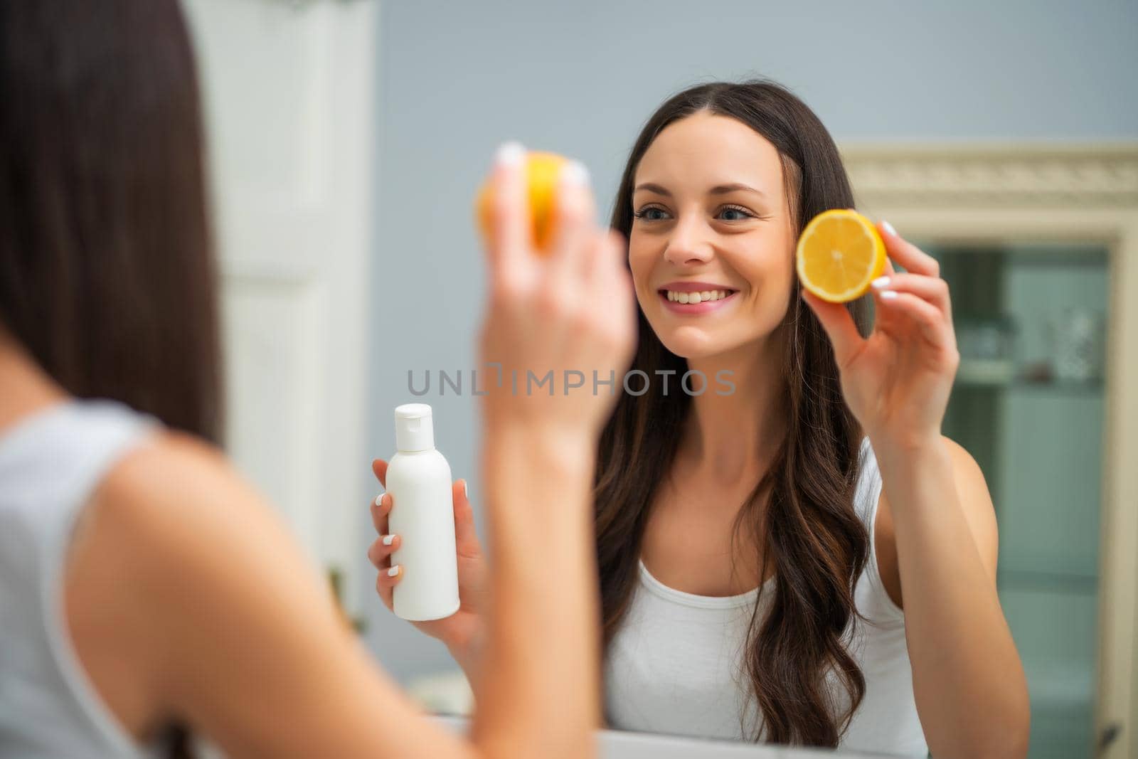 Beautiful young woman is holding lemon and skin cream.