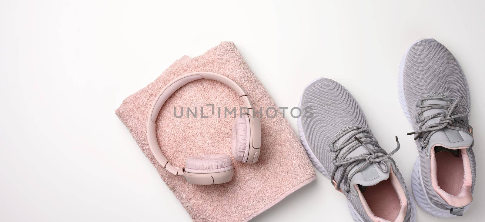 pair of gray textile sneakers, wireless headphones and a textile pink towel on a white background. Set for sports, running