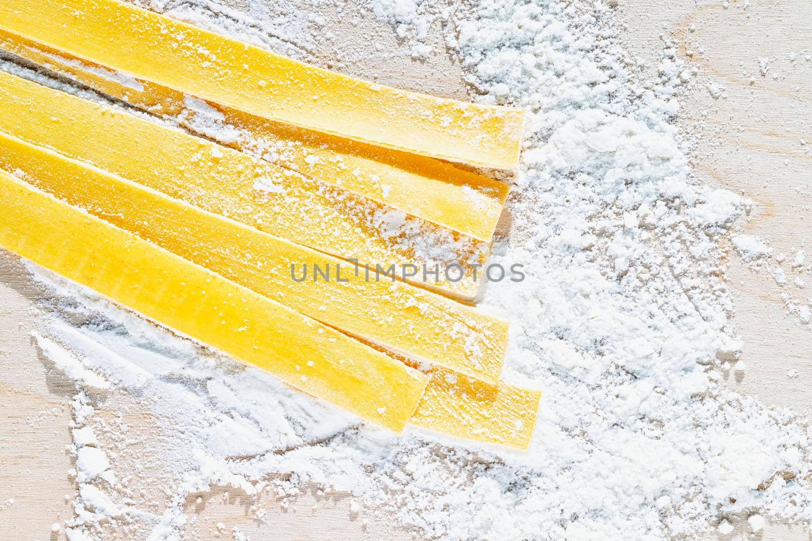 Large flat egg  pasta pappardelle with flour on wooden background , uncooked pasta