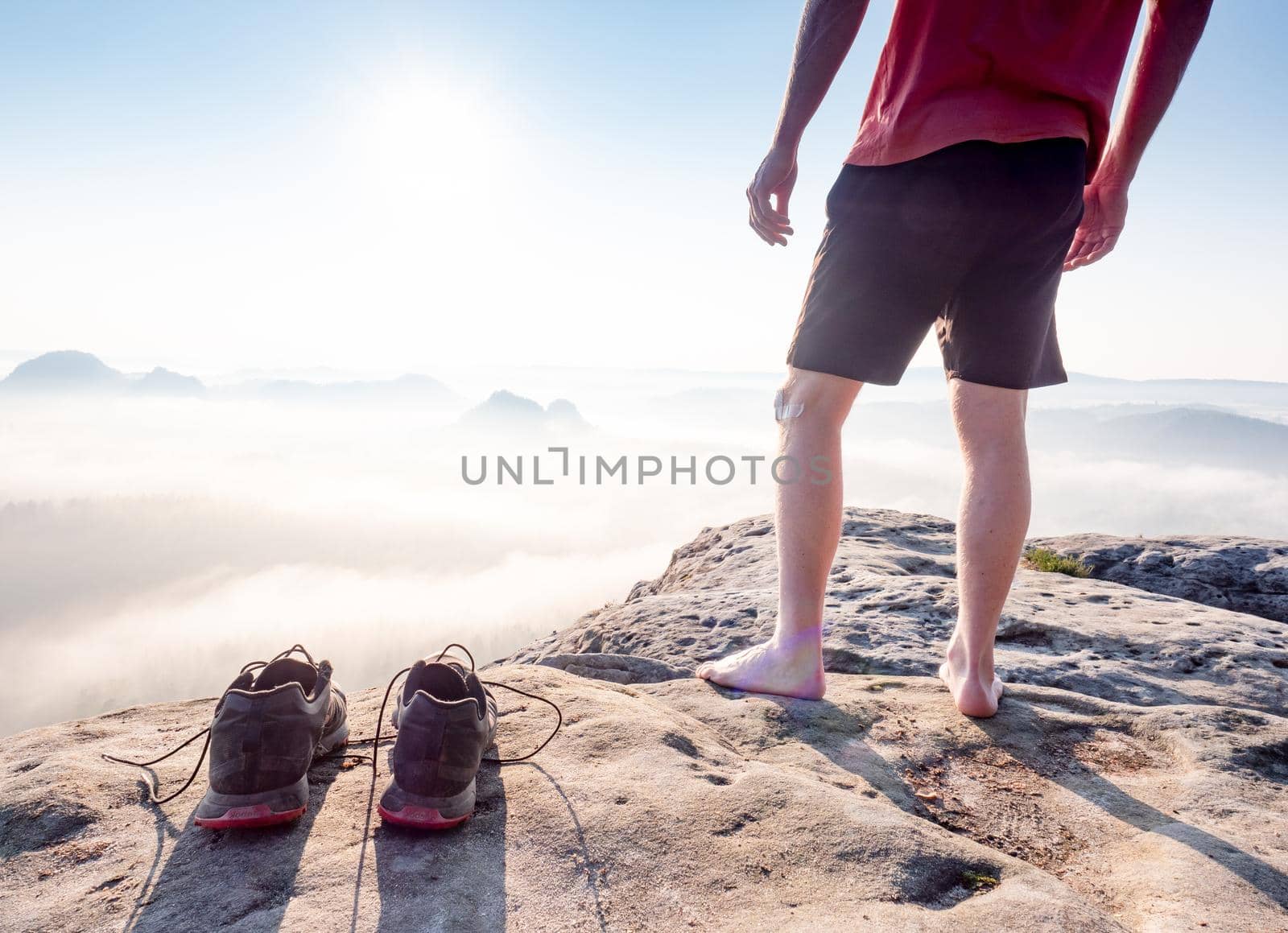 Middle age healthy male body with naked legs on mountain peak rock.  Satisfy hiker enjoy view. Tall man on rocky cliff watching down to landscape. 