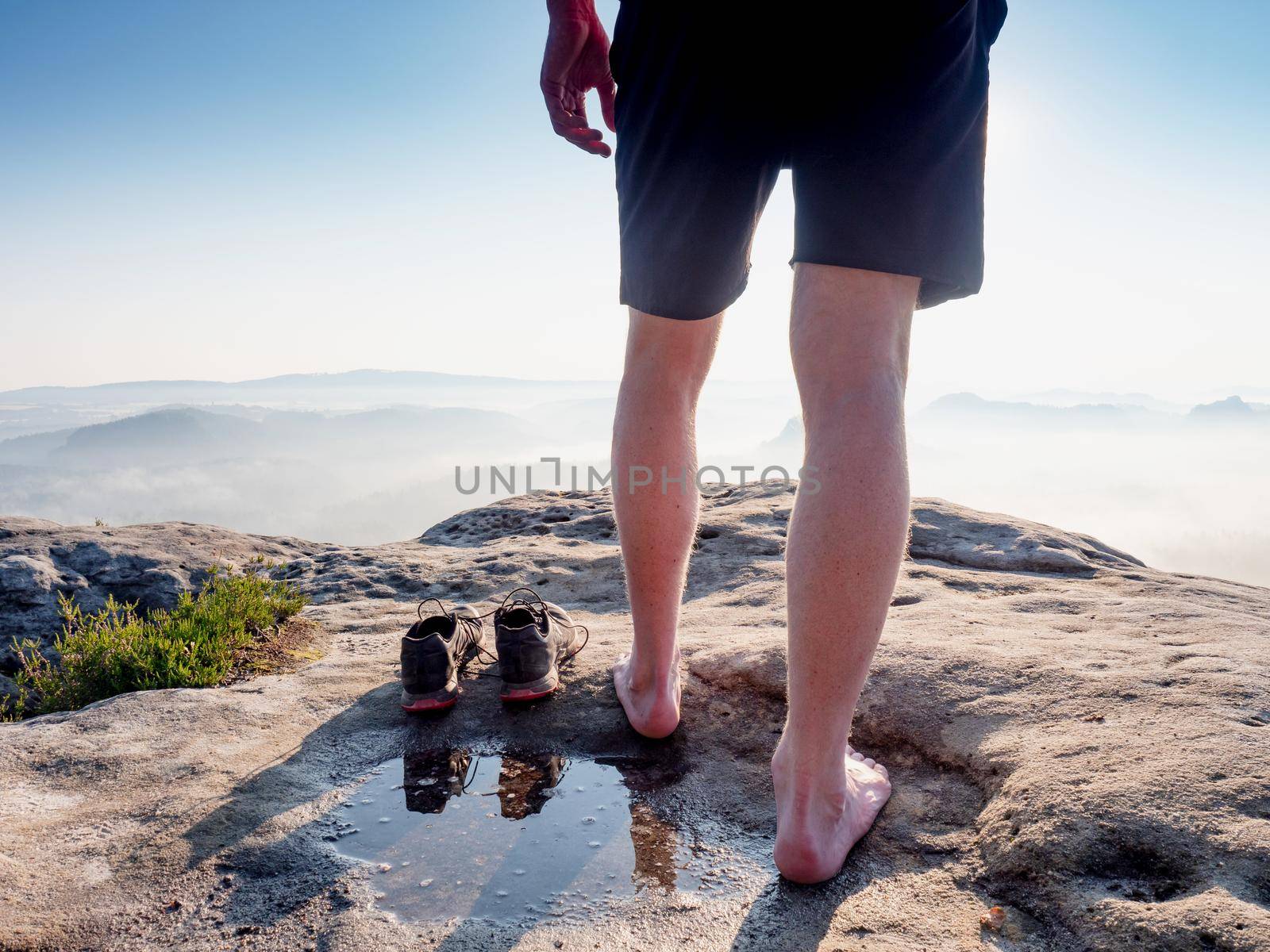 Hiker next to taken off shoes and water puddle on sandstone rock edge enjoy misty landscape view