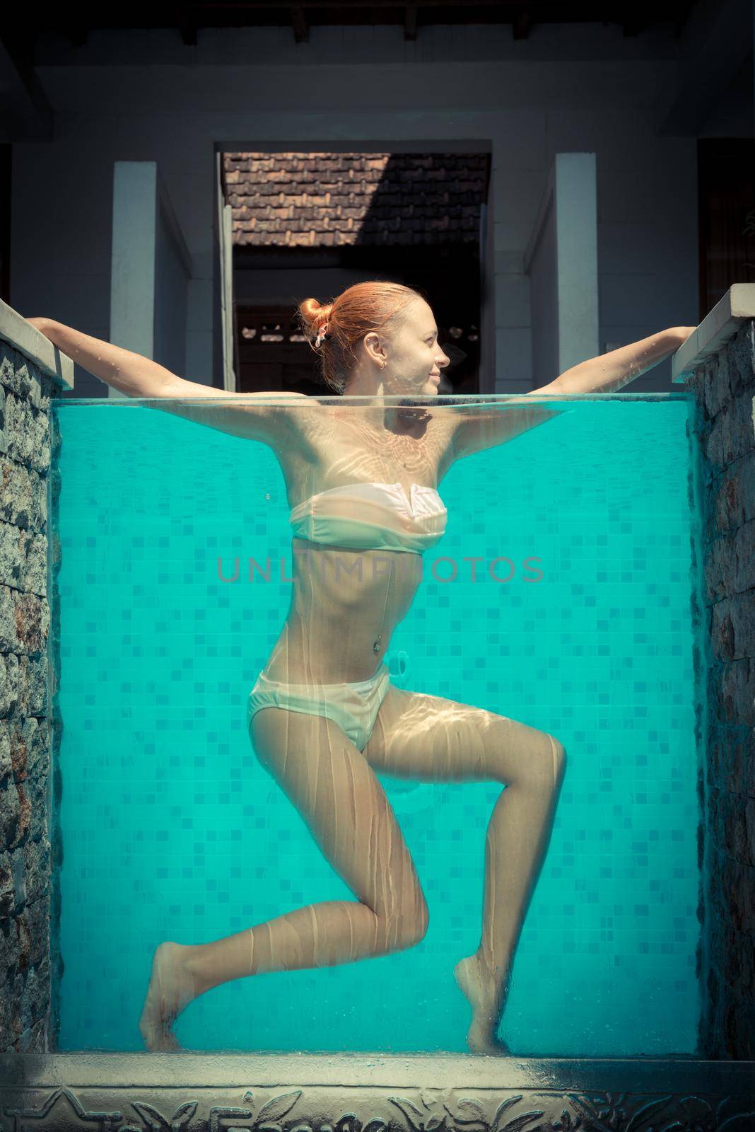 Attractive slim red woman in blue swimming pool with transparent wall