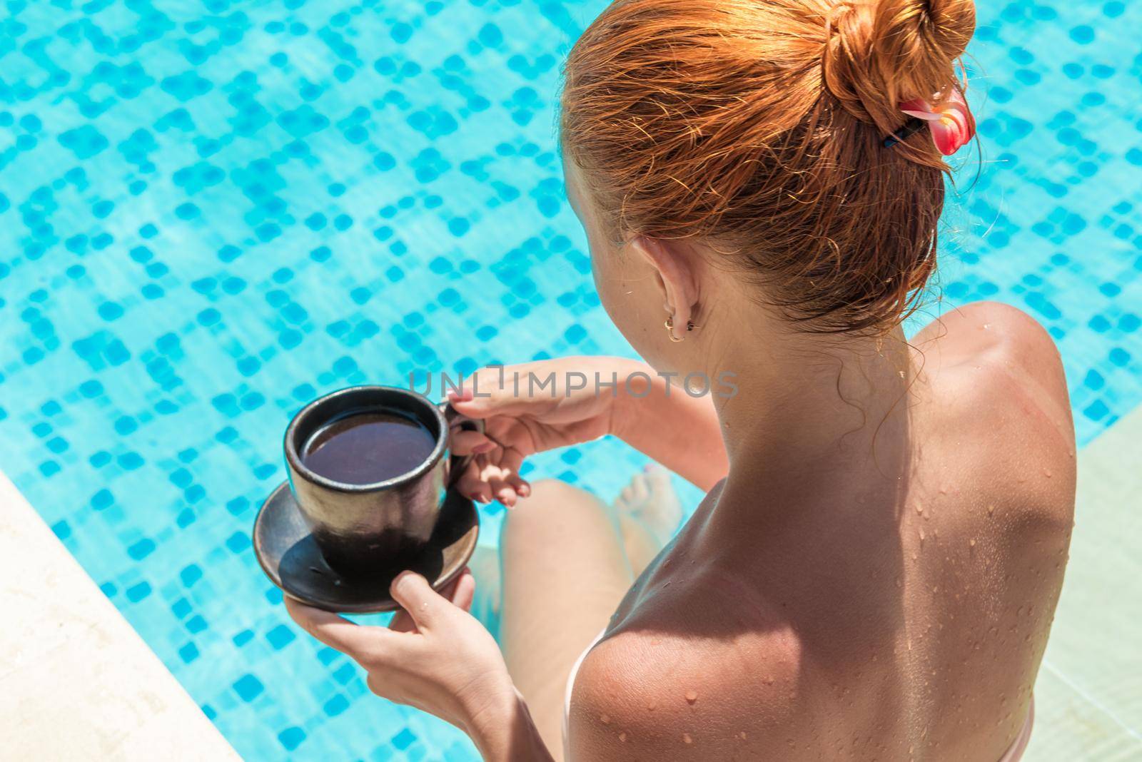 Young woman wearing swimsuit enjoying coffee near swimming pool at exotic location