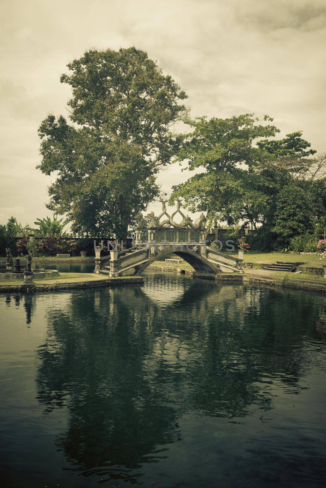 Green park with clean lake and stone balinese style arch bridge, Tirtaganga, Bali