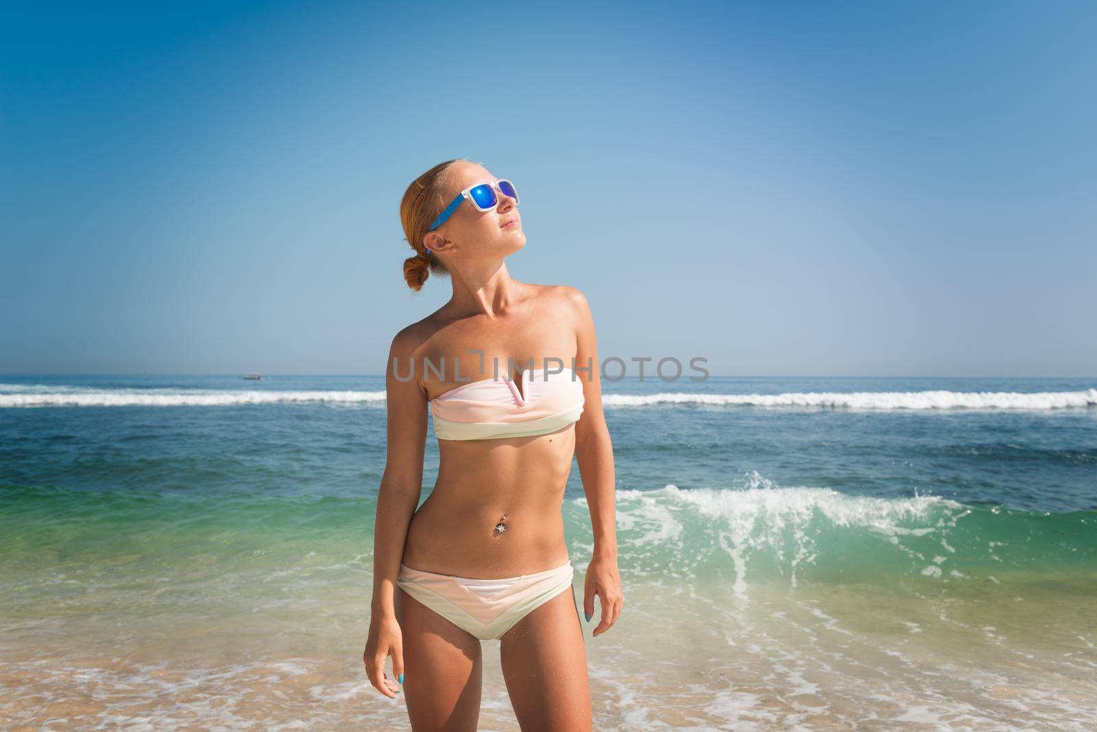 Young slim woman wearing bikini and sunglasses at the ocean beach