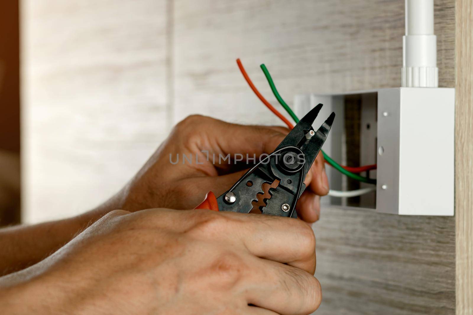 Electrician is stripping electrical wires in a plastic box on a wooden wall to install the electrical outlet.