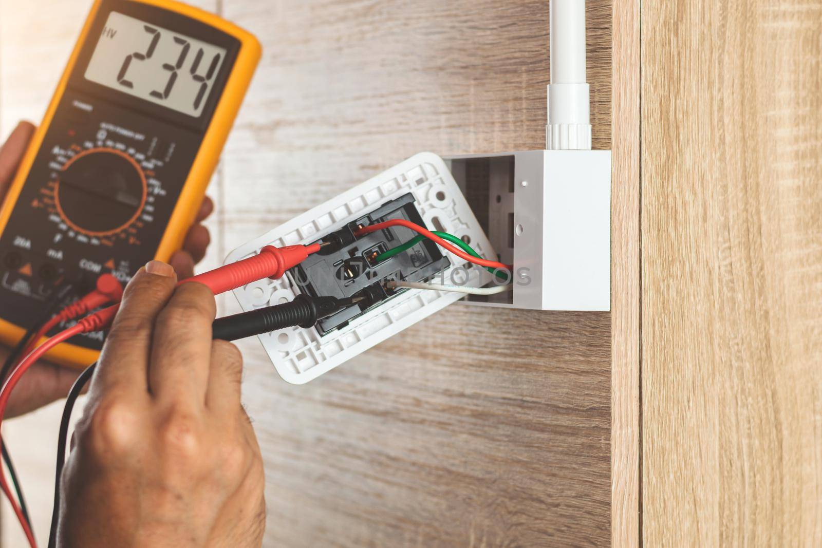 Remove the power electric plug socket from the outlet box on the wooden wall to measure the voltage with a digital meter. by wattanaphob