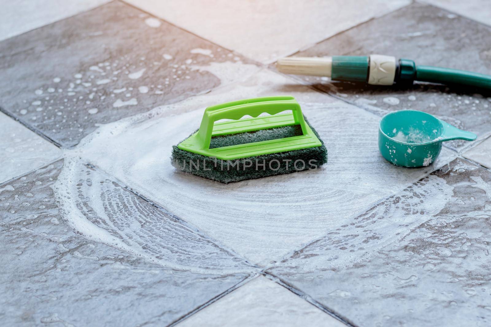 Close up the green plastic brush for scrubbing and cleaning the floor is placed on the wet tile floor and foamed with detergent. by wattanaphob