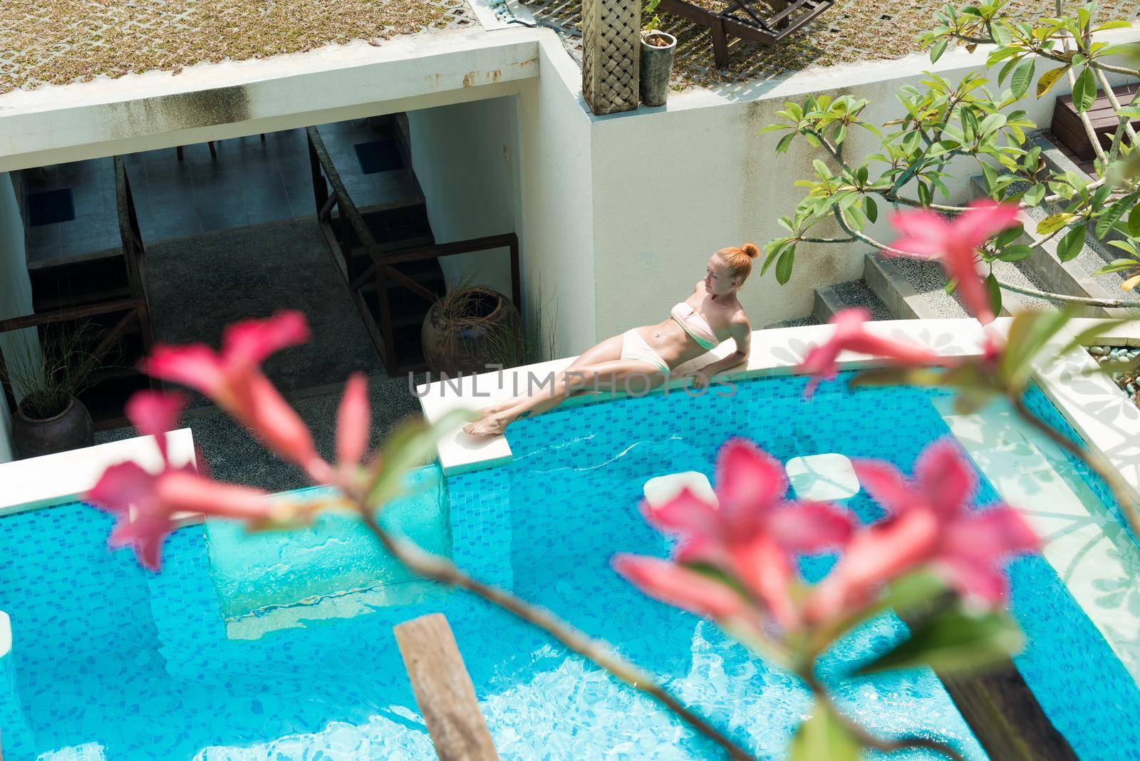 Young woman wearing swimsuit relaxing near swimming pool at exotic location