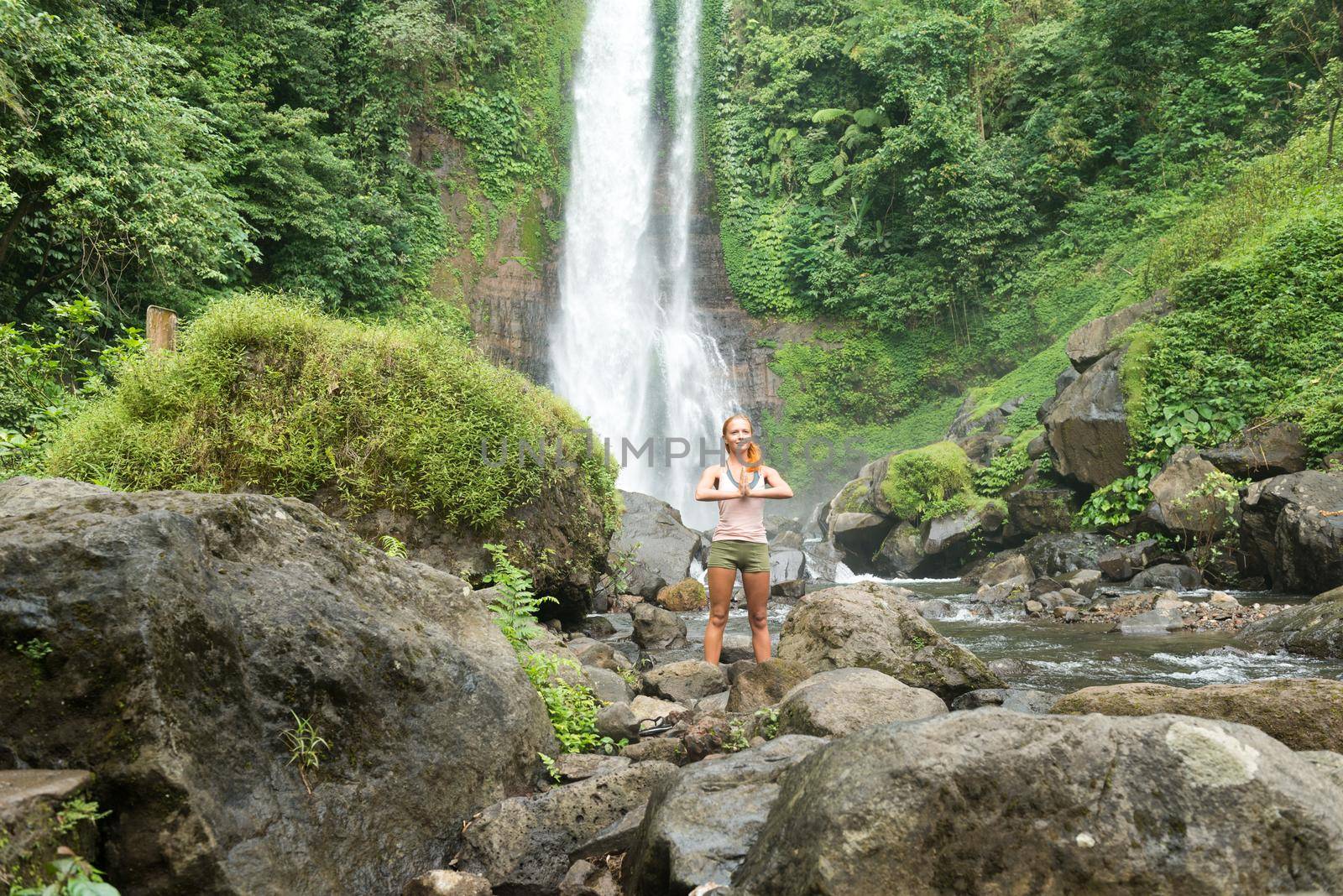 Young woman practicing yoga by the waterfall by nikitabuida